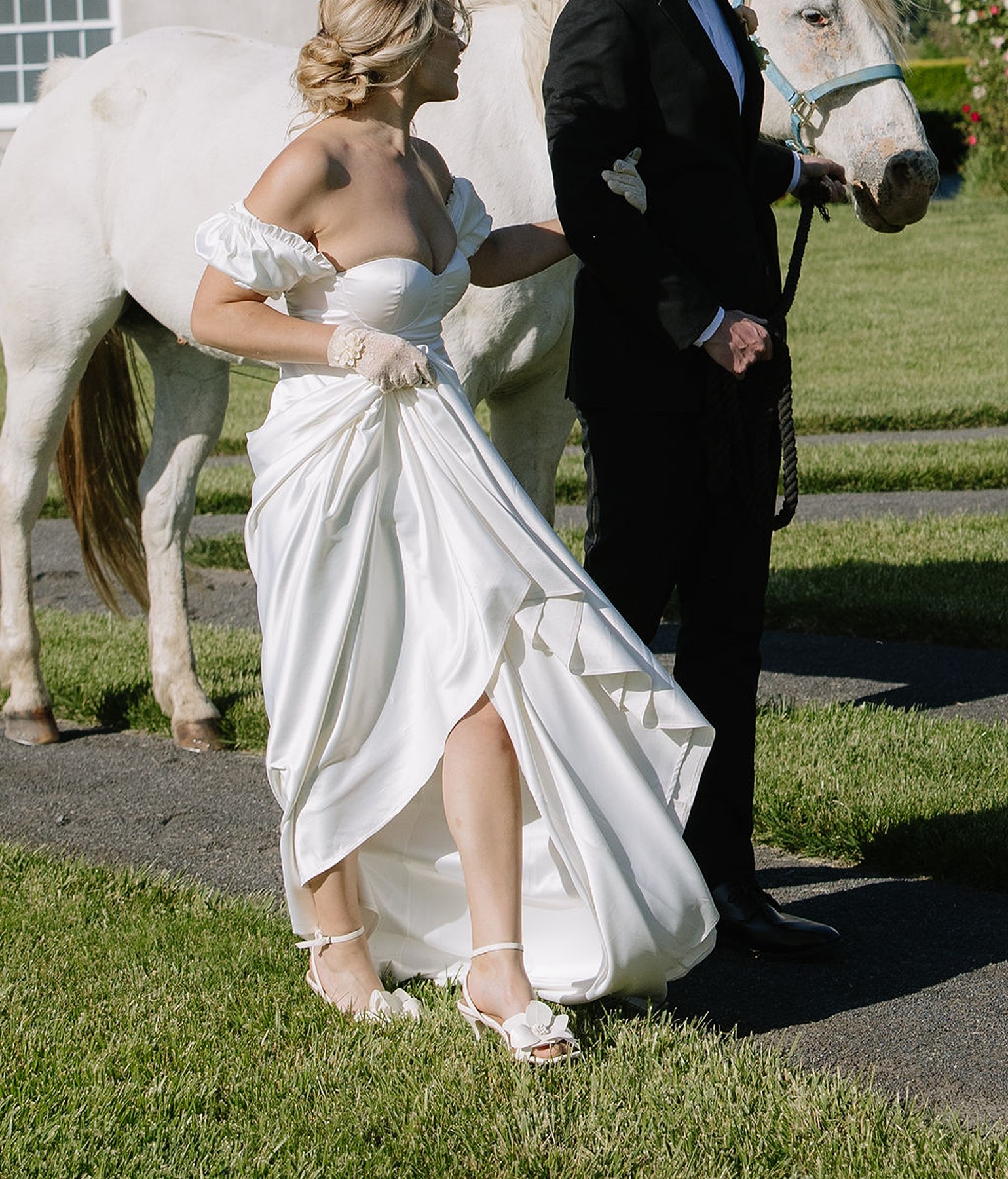 Bride holding her dress and her groom's arm, who is walking holding a horse