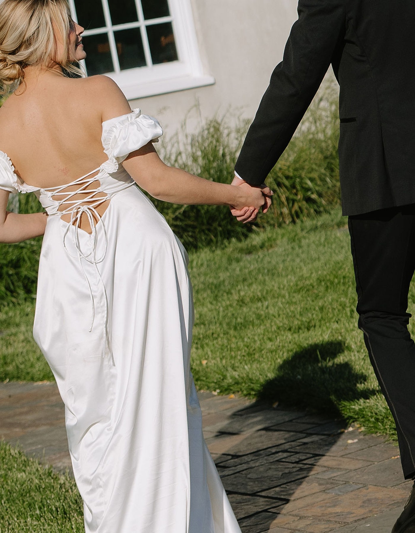 A couple holding hands walking away from the camera towards Cavaignac, a country estate, with bride wearing a dress with a corset lace up. 