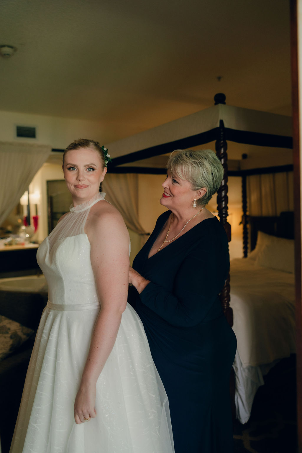 Mother of the bride helping bride put on dress during wedding getting ready photos