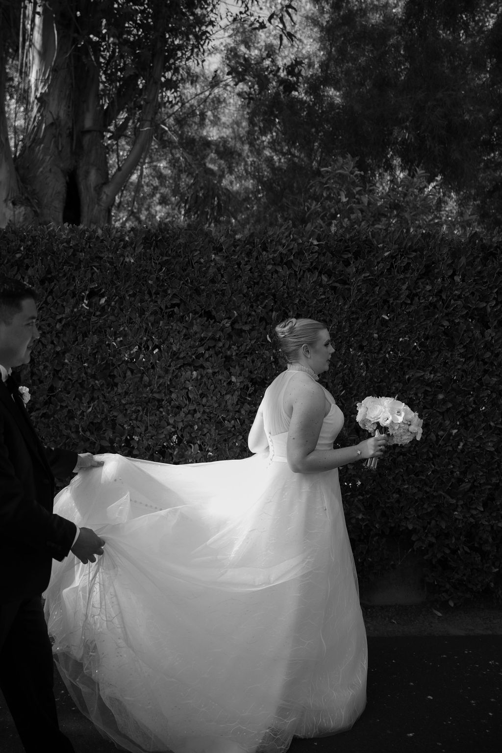 Candid wedding photo of groom carrying bride's wedding dress train