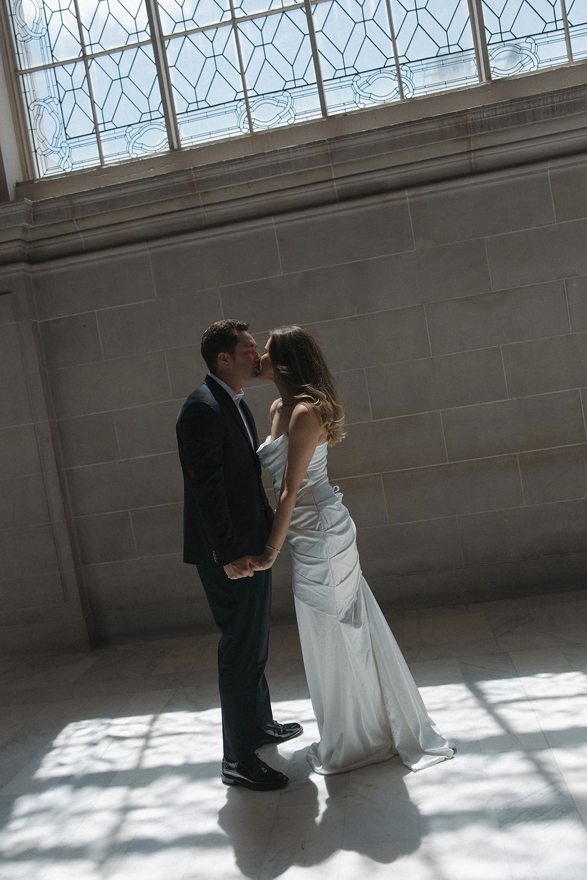 Couple kissing underneath an ornate window with the light shining through for their city hall elopement