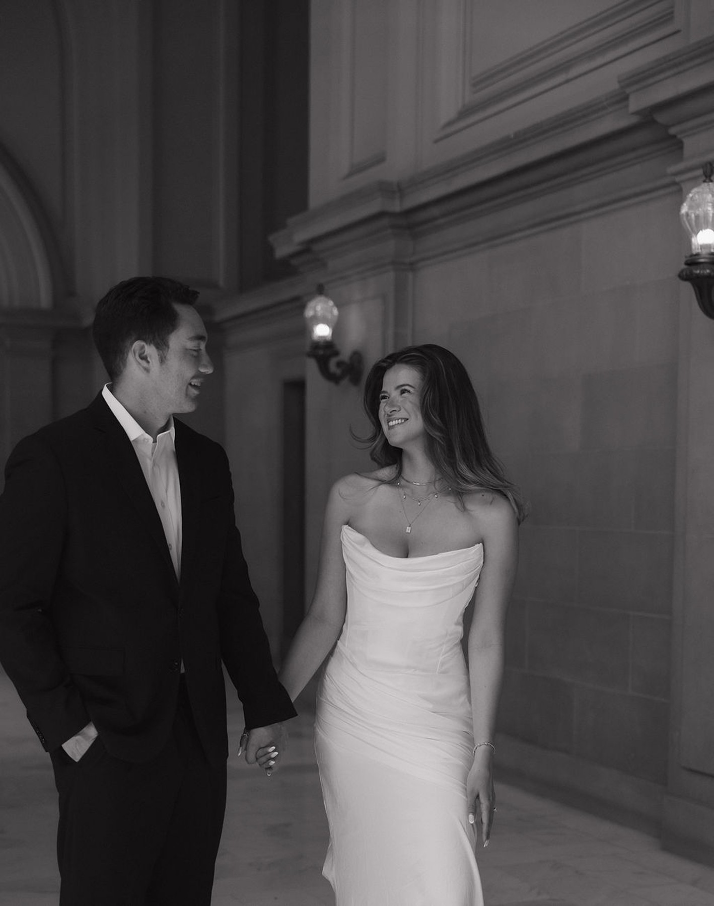Black and white wedding photo of couple smiling at each other in a hallway at their courthouse wedding
