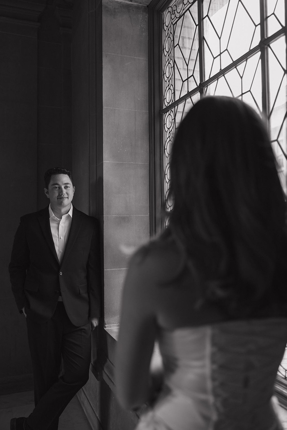 Editorial photo of groom staring smiling at bride with camera facing bride's back