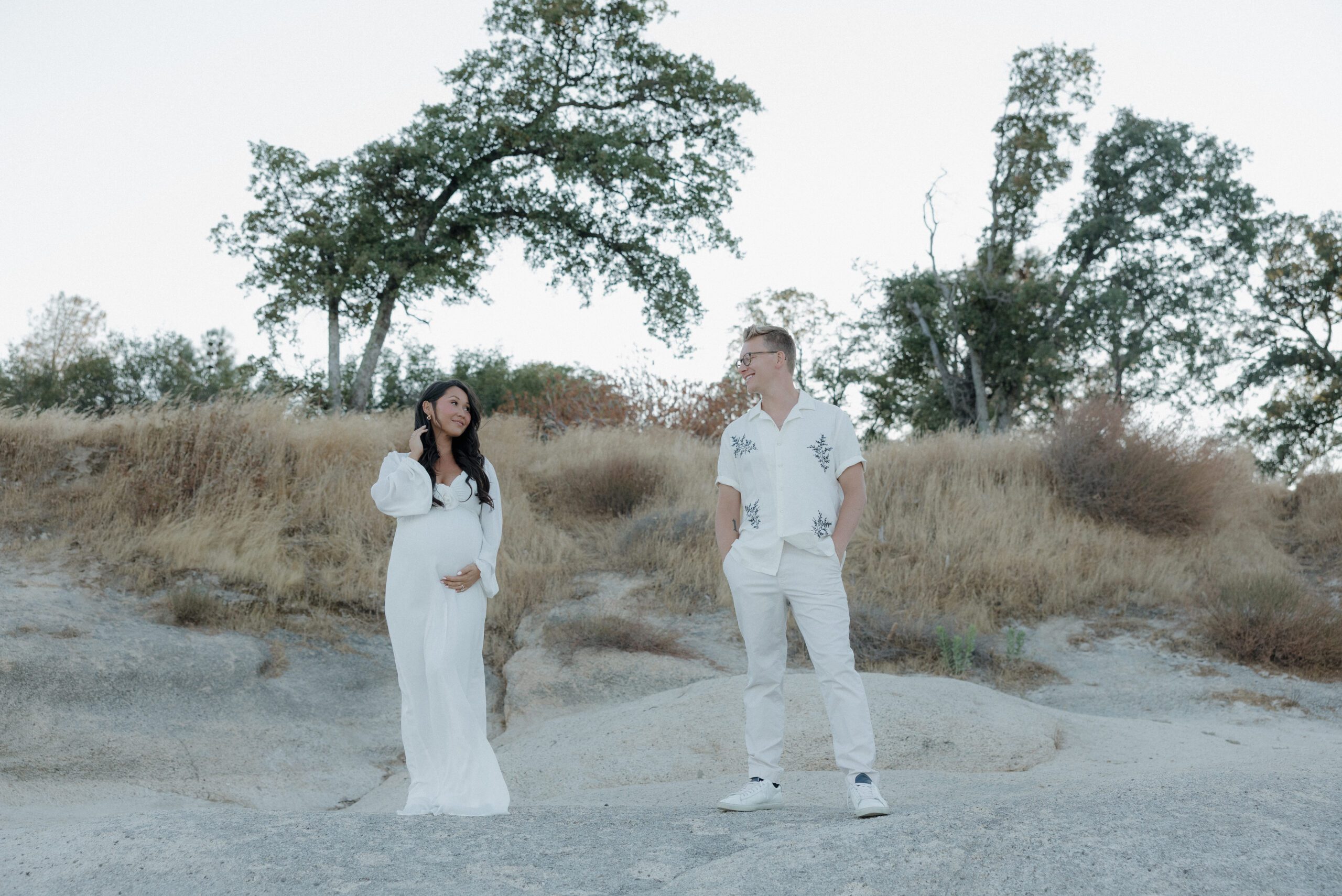A couple smiling at each other while wife holds her baby bump