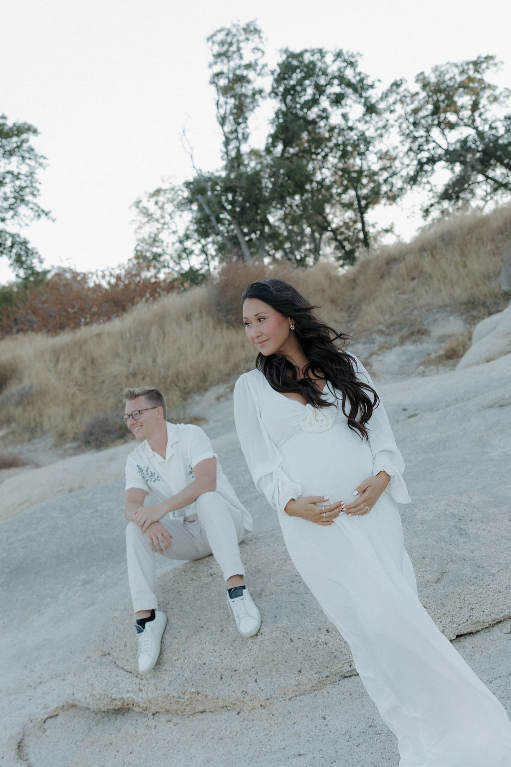 Man sitting behind his wife who is holding her baby bump as a maternity photo pose