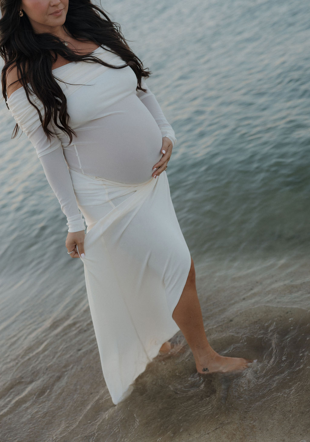 An editorial maternity photo of the mother walking through the lake while holding her baby bump