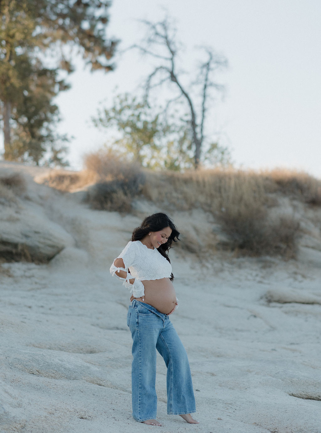 A woman holding her baby bump and looking down at it, as a maternity photoshoot pose