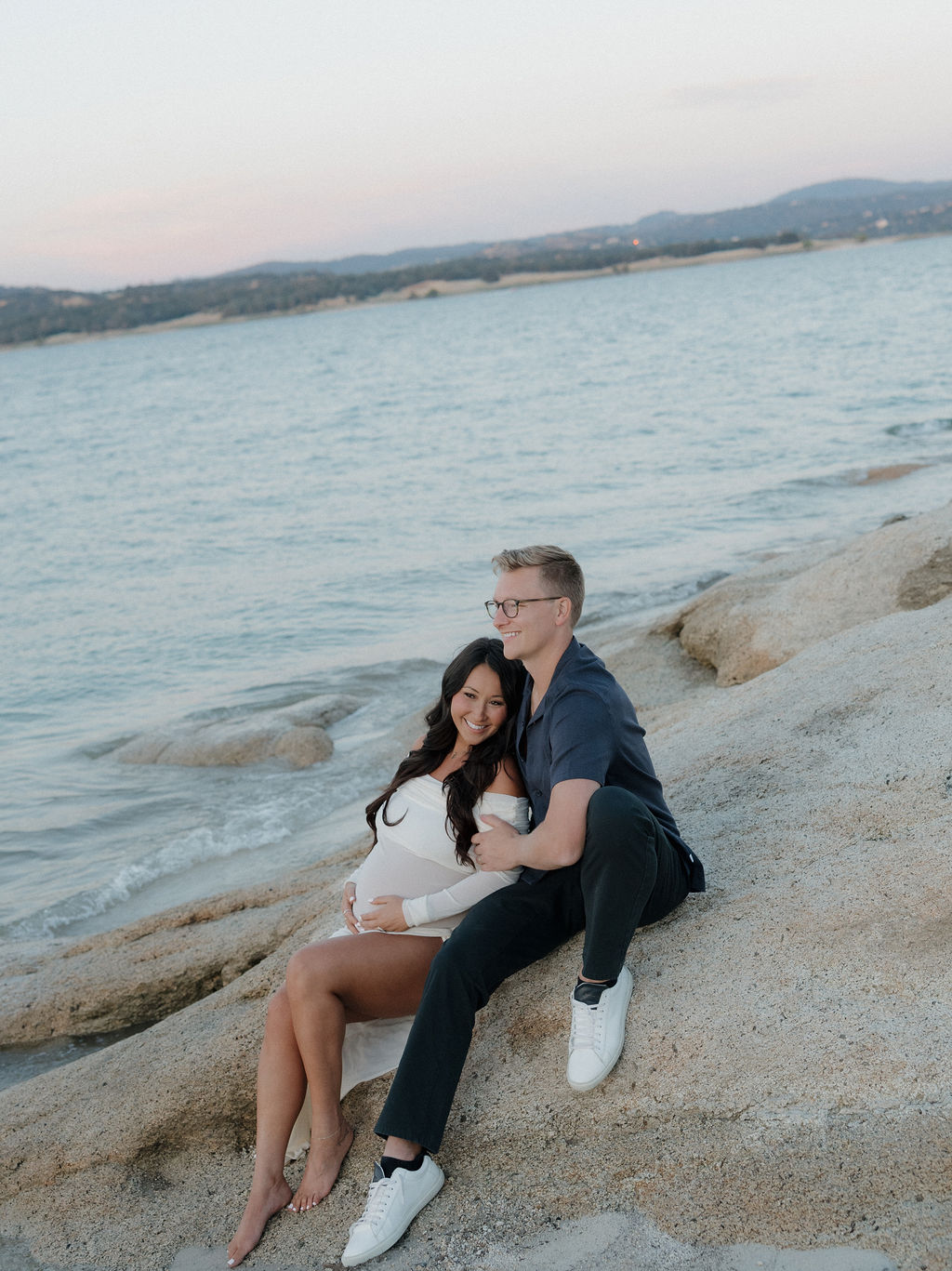 A woman holding her baby bump sitting leaned against her husband