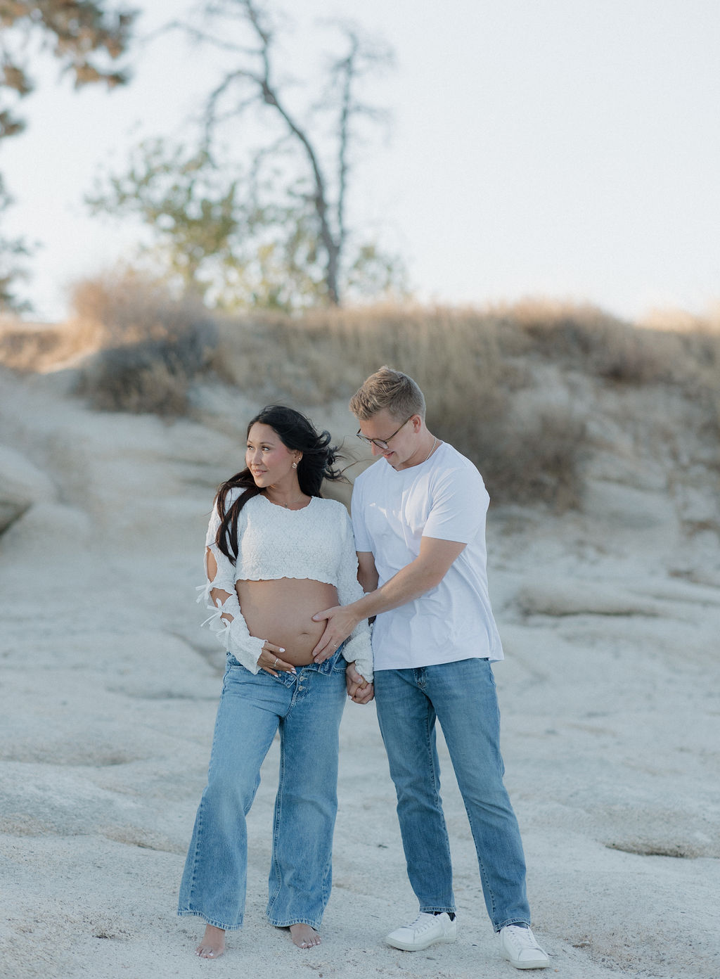 A couple standing in front of sand dunes at Folsom Lake holding their baby bump