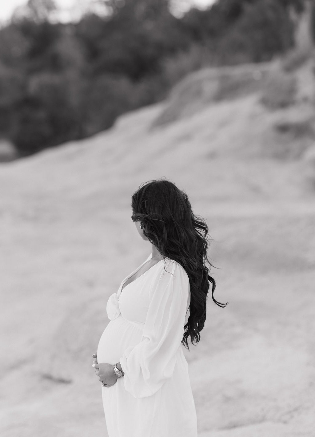 A black and white photo of woman holding her baby bump with her head turned away from the camera, as a maternity photoshoot pose