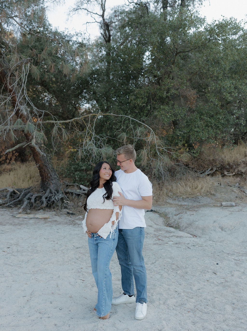 A couple posing for a maternity photo, with woman looking up at her husband