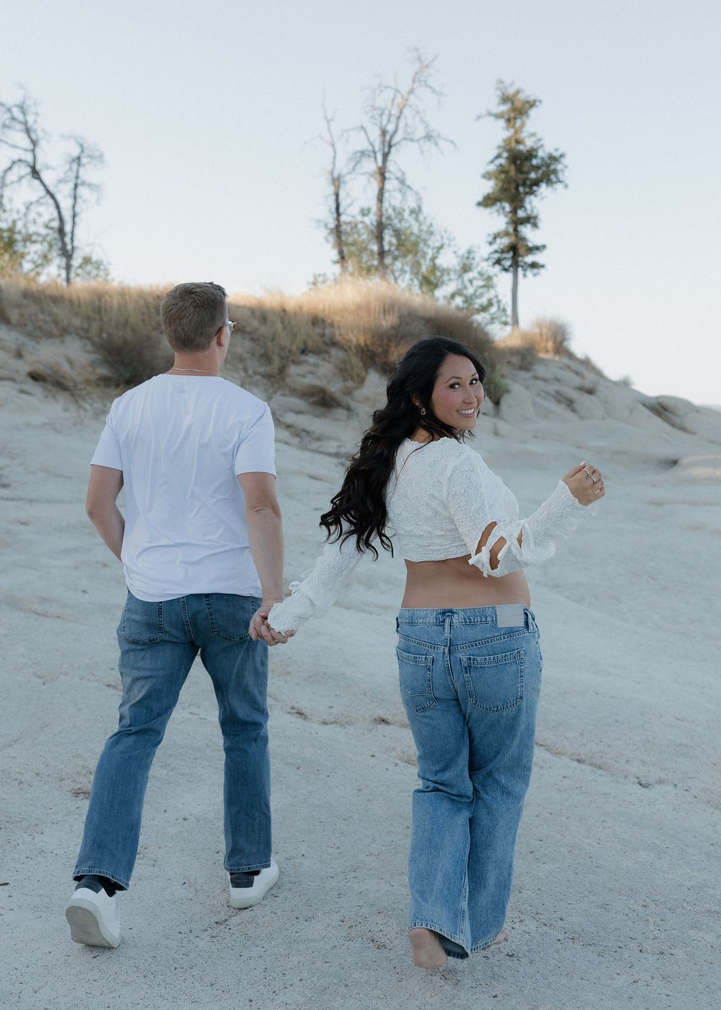 A man and woman wearing white turns walking away from the camera during a maternity photoshoot