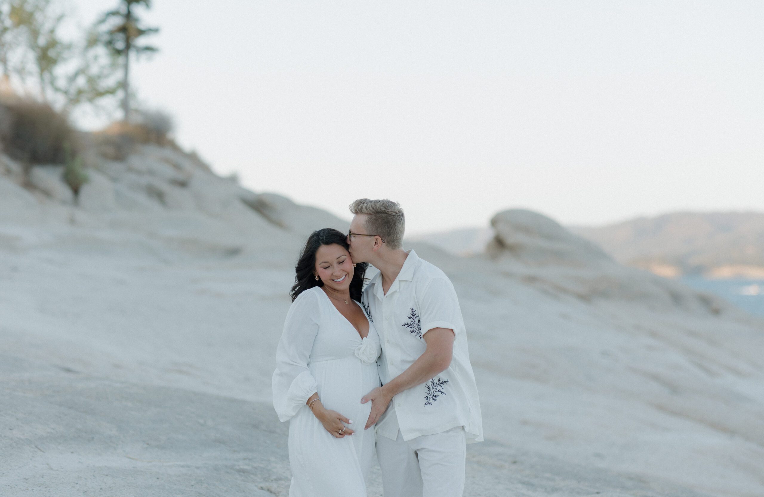 A man kissing his wife, who is holding her baby bump, on the temple