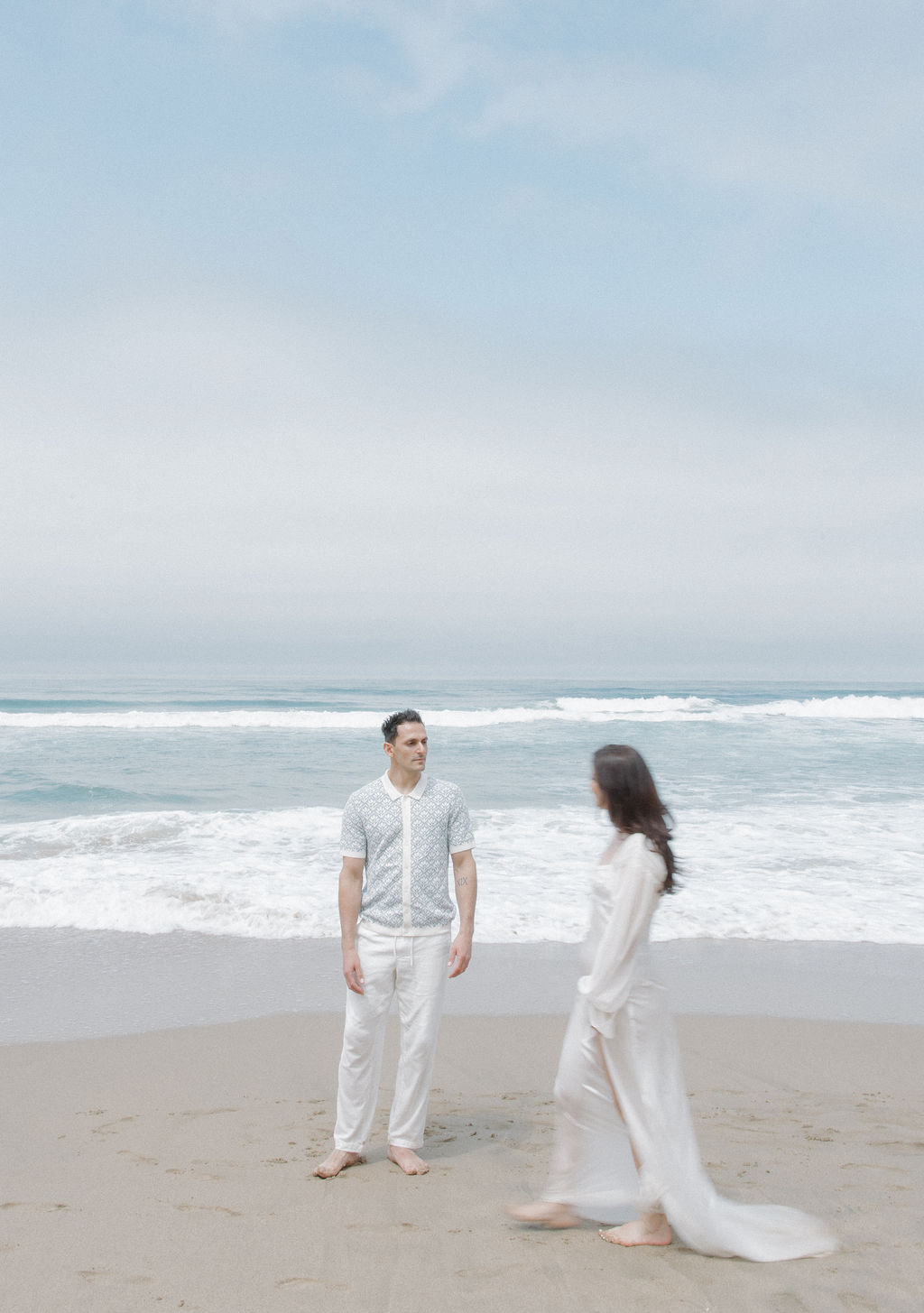 Woman walking around man standing on the beach, as an editorial engagement photo pose
