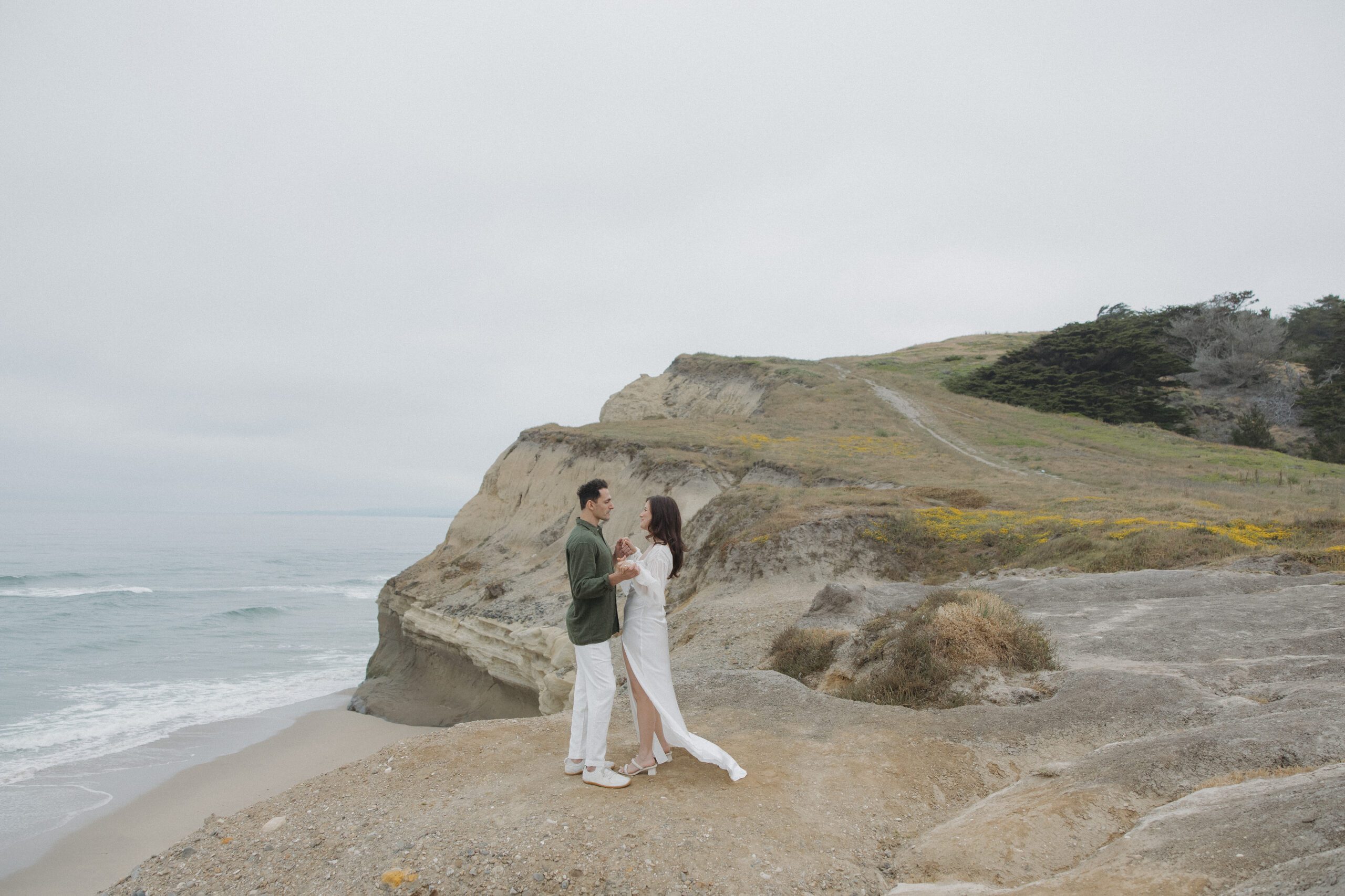 Couple standing on a cliff at Half Moon Bay for their engagement photos
