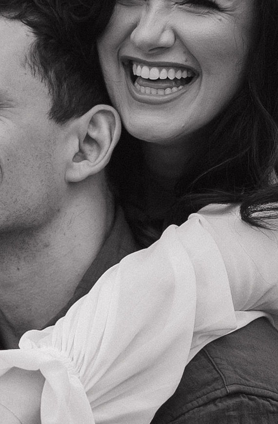 Black and white up close photo of woman laughing while hugging her fiancé from behind