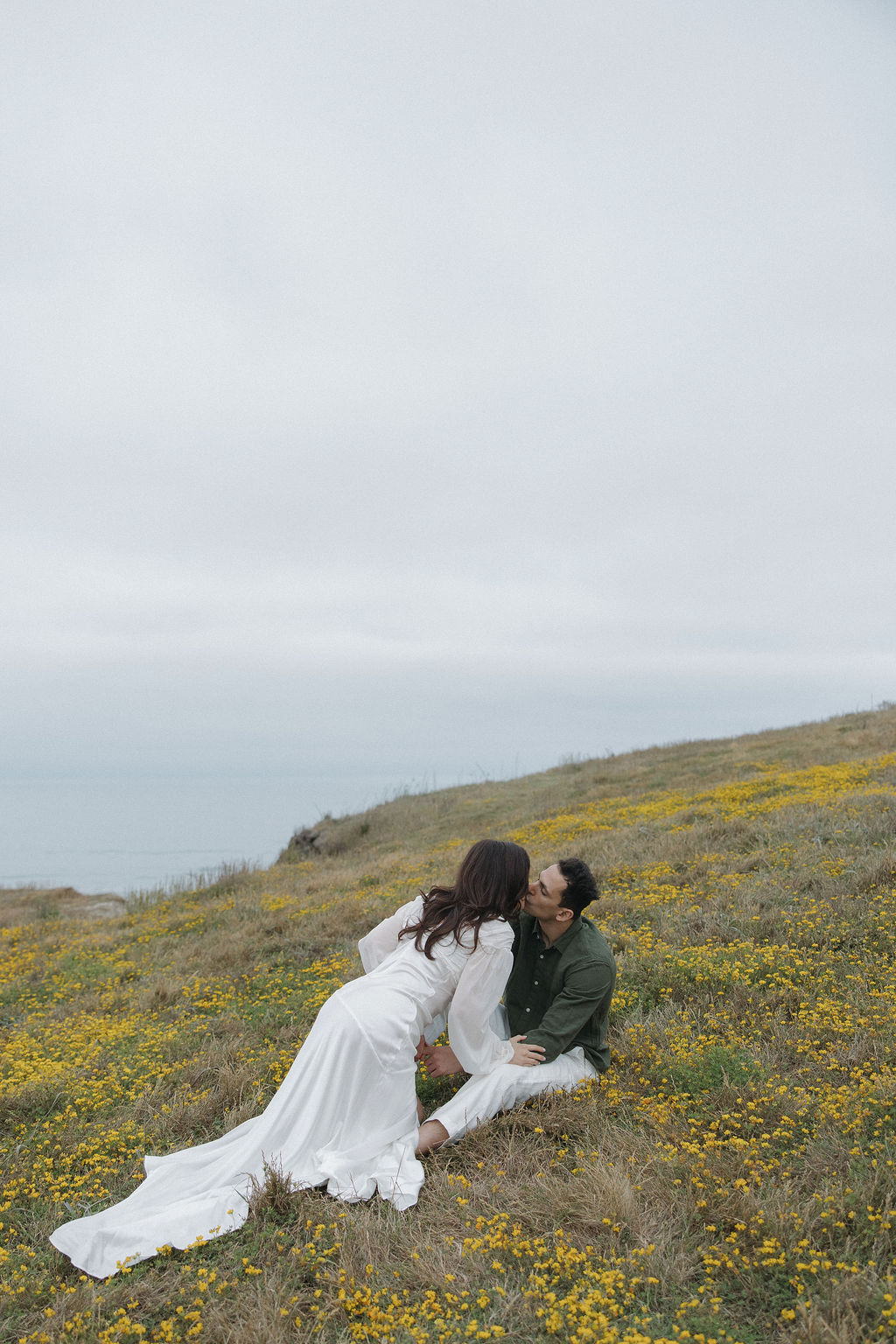 Couple kissing on the ground in a field with yellow flowers