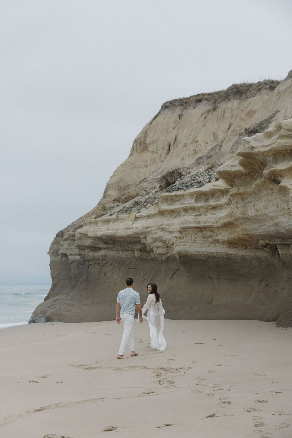 Couple walking on the beach with a cliff behind them