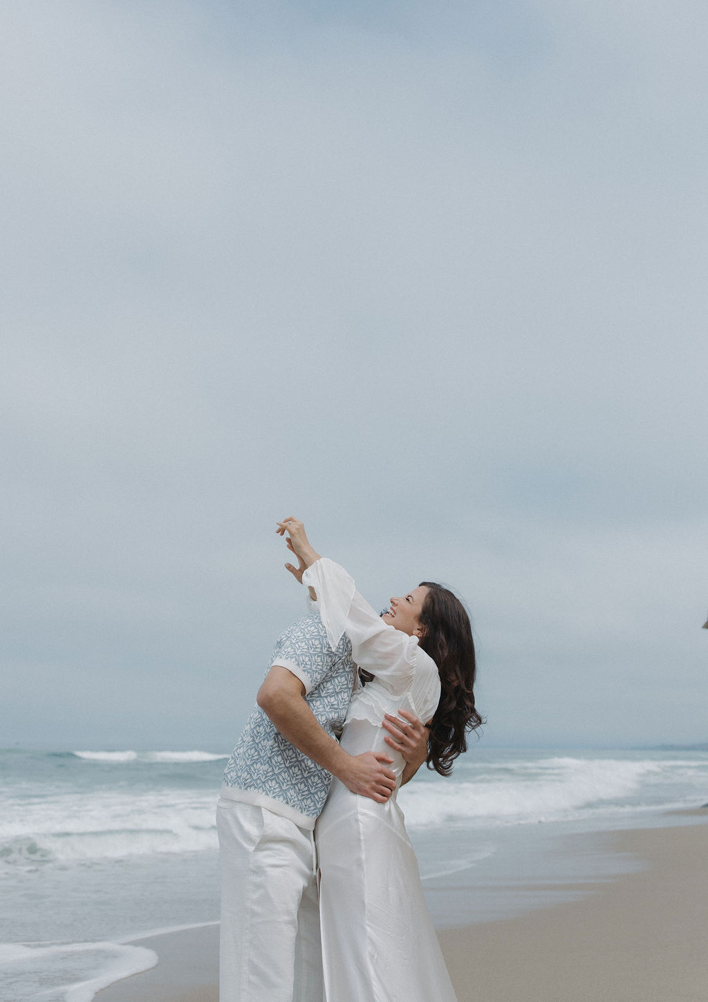 Couple hugging on the beach during their beach engagement photoshoot, with girl's arms reaching up