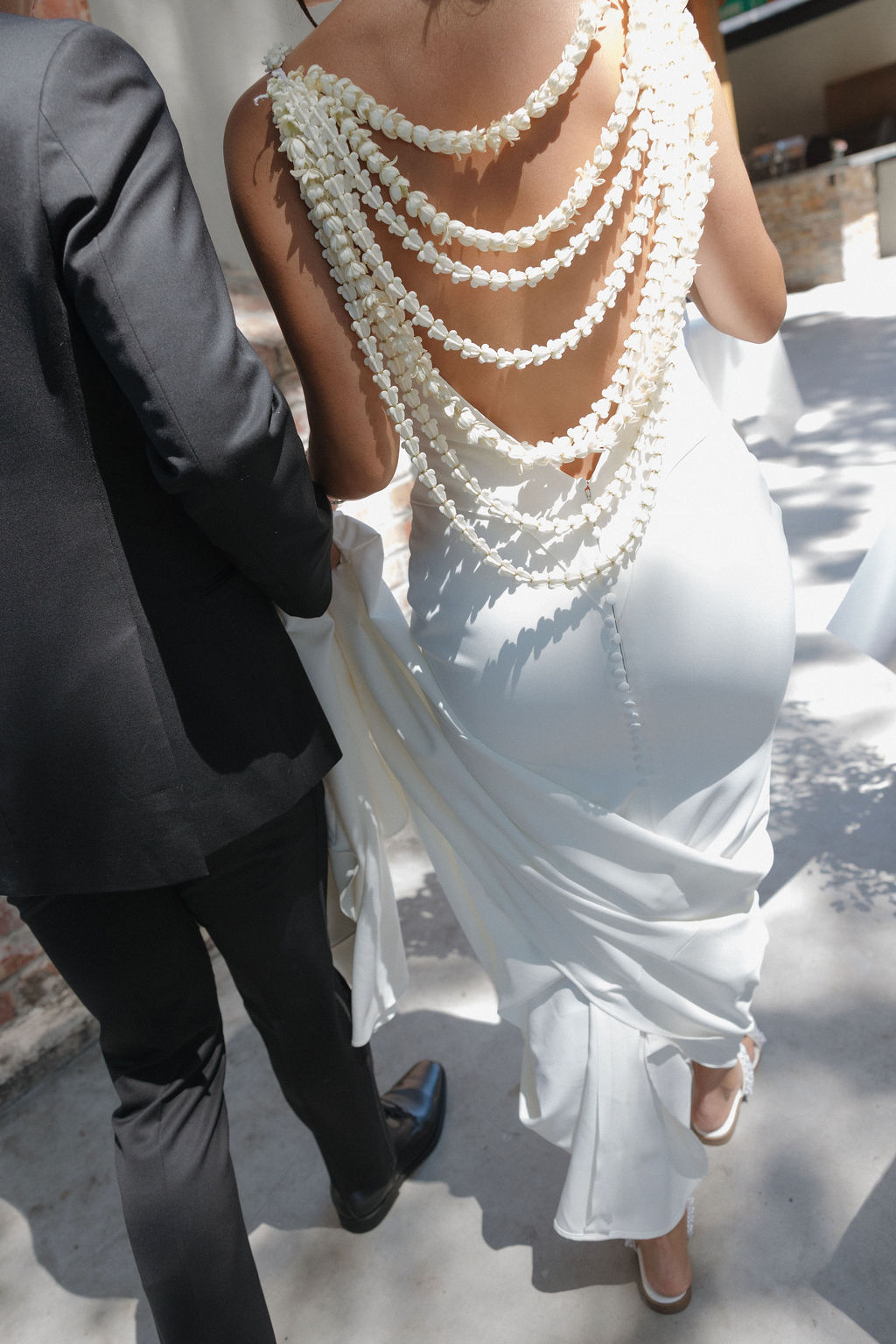 The back of bride's wedding dress with an open back with strings of Hawaiian flowers