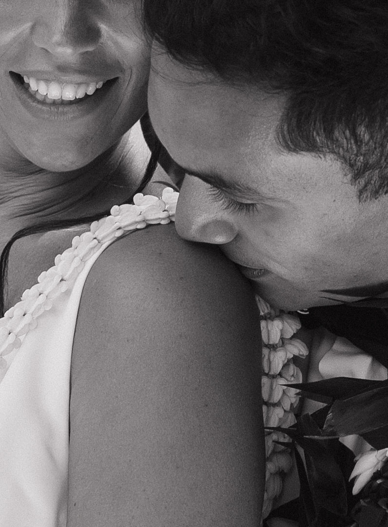 Black and white editorial wedding photo of groom kissing bride's shoulder