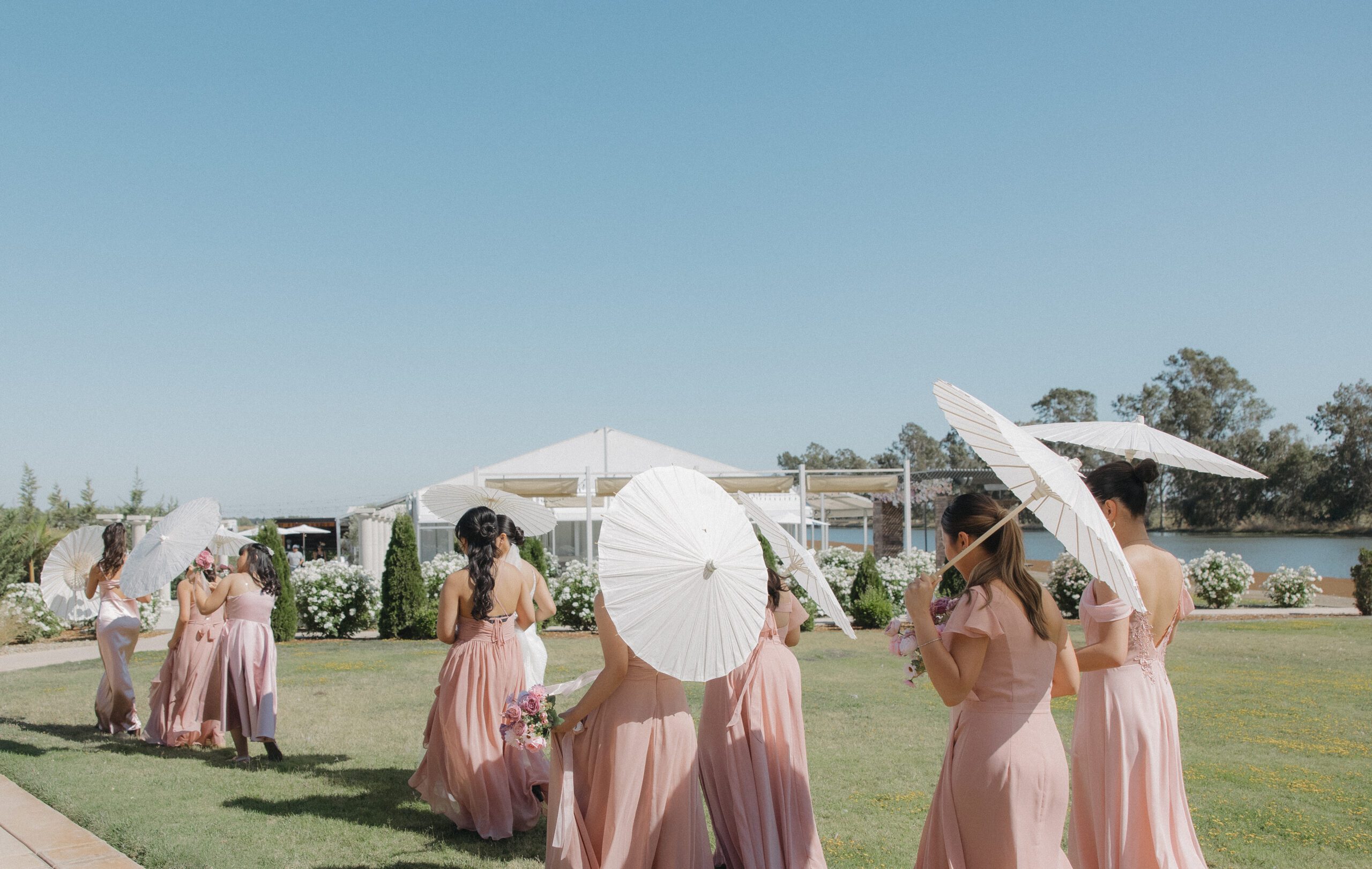 Bridesmaids walking in pink bridesmaid dresses and carrying parasols in candid wedding photo