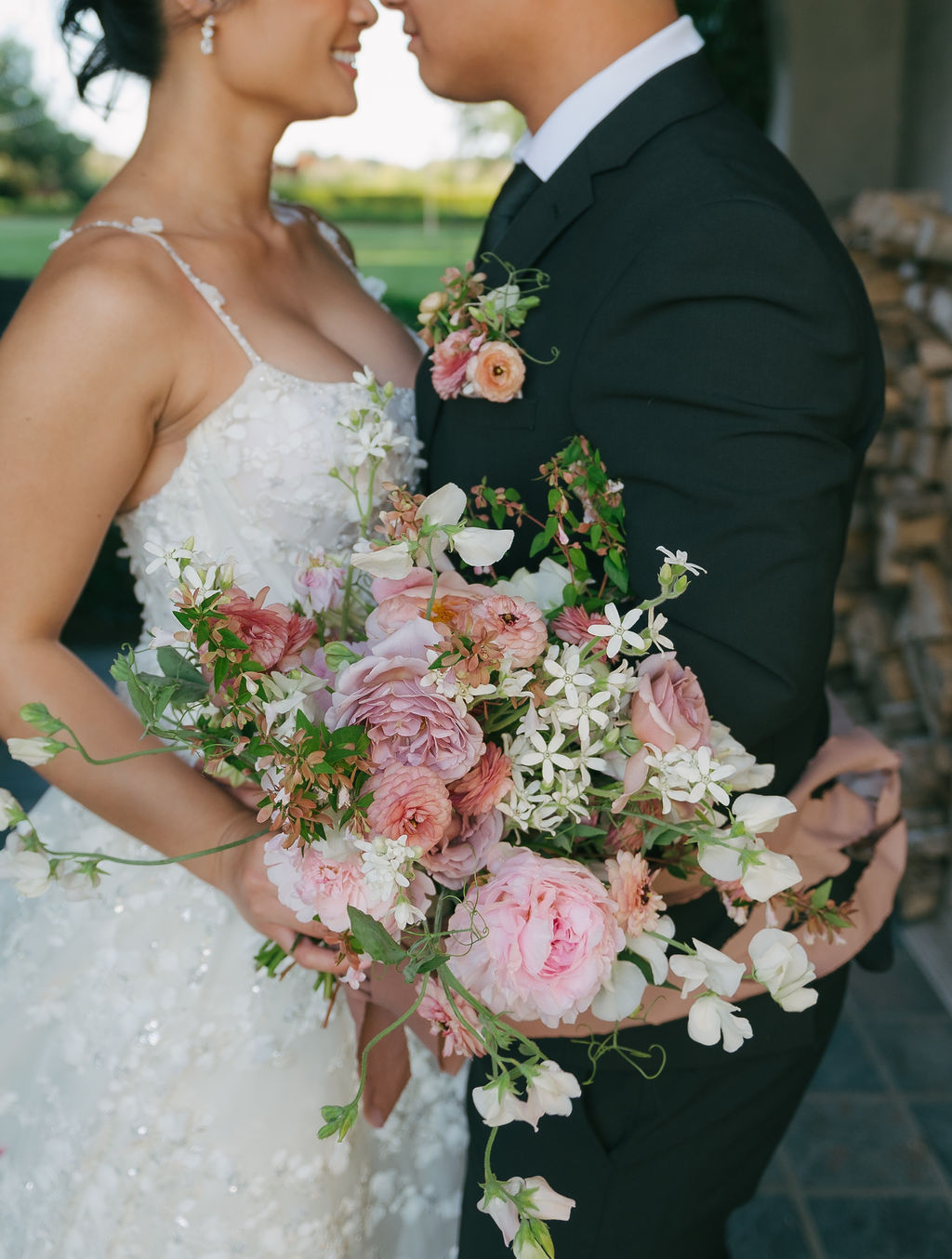 A pink and white wedding bouquet with bride and groom out of focus behind it
