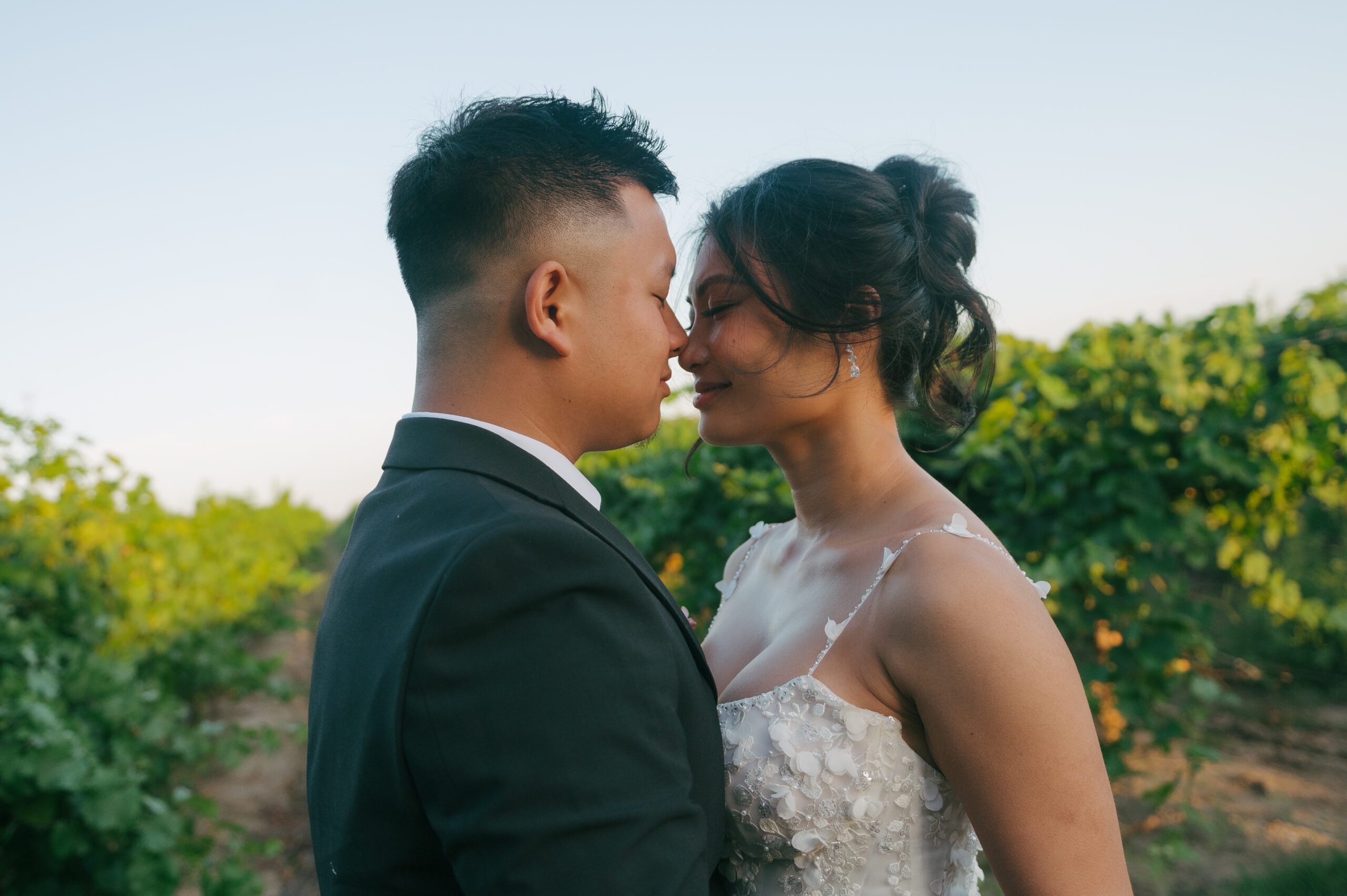 Bride and groom standing touching noses in a vineyard