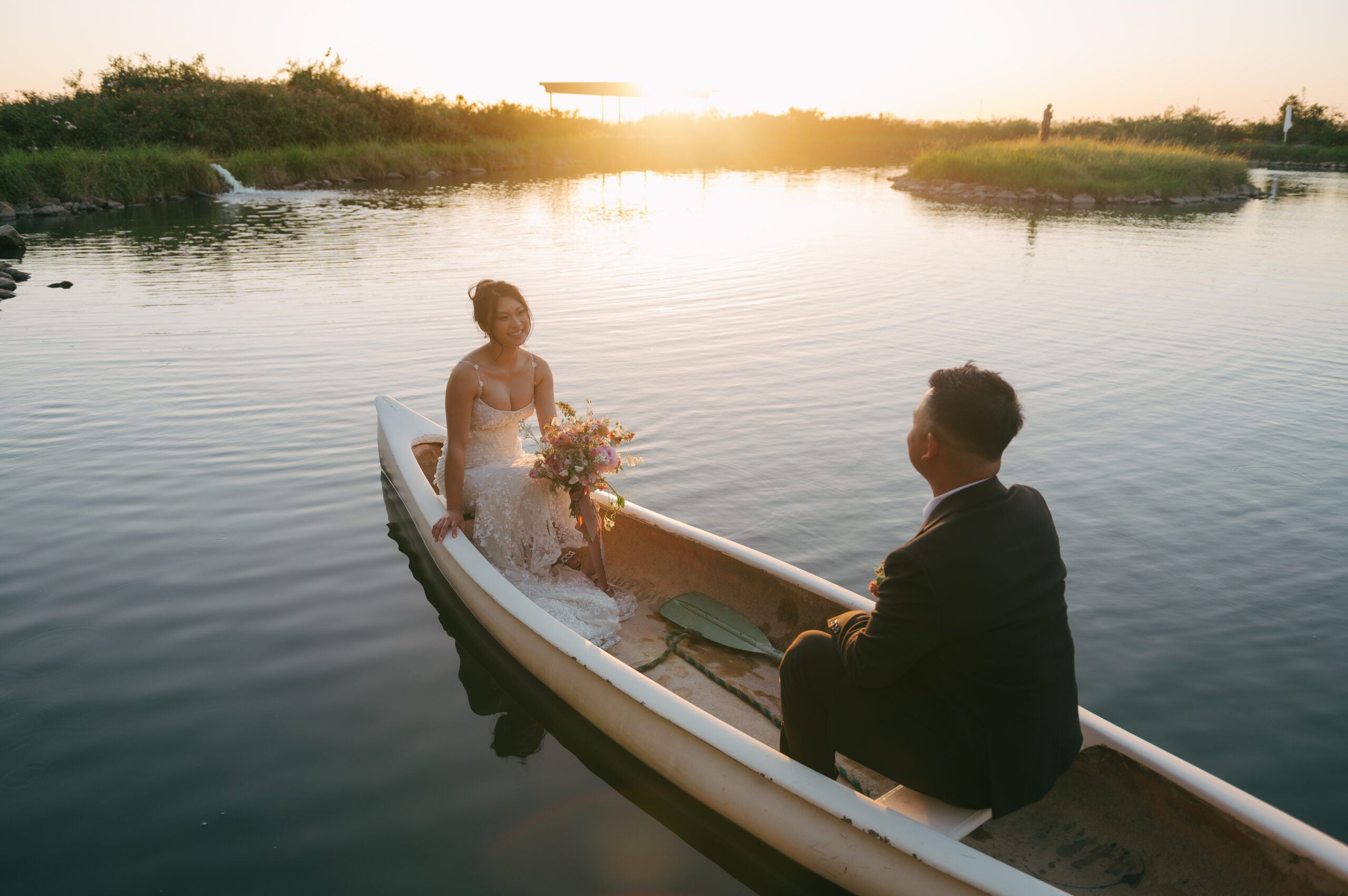 Bride and groom in a rowboat on a pond during golden hour wedding photos
