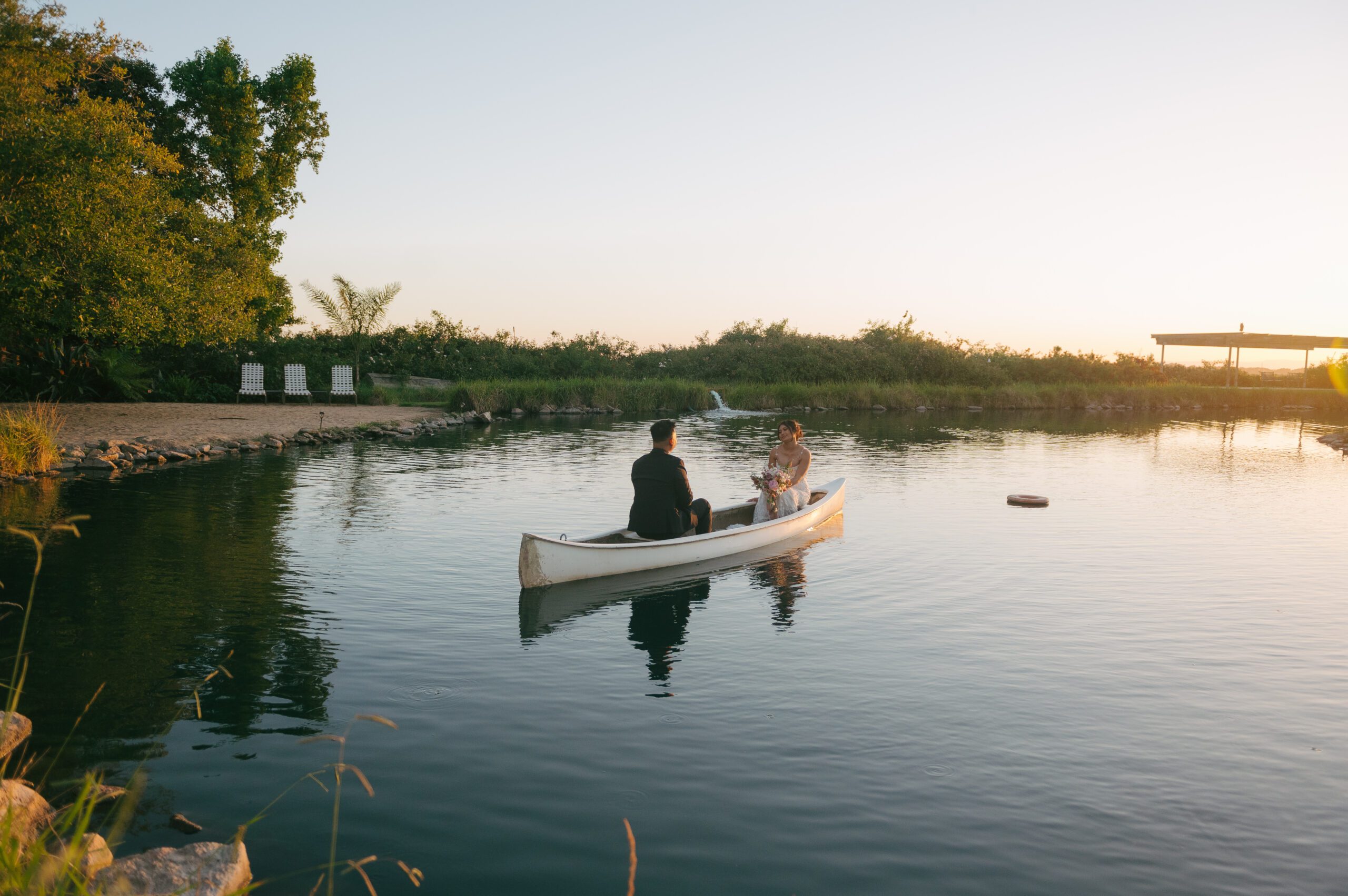 Bride and groom in a rowboat on a pond during golden hour wedding photos