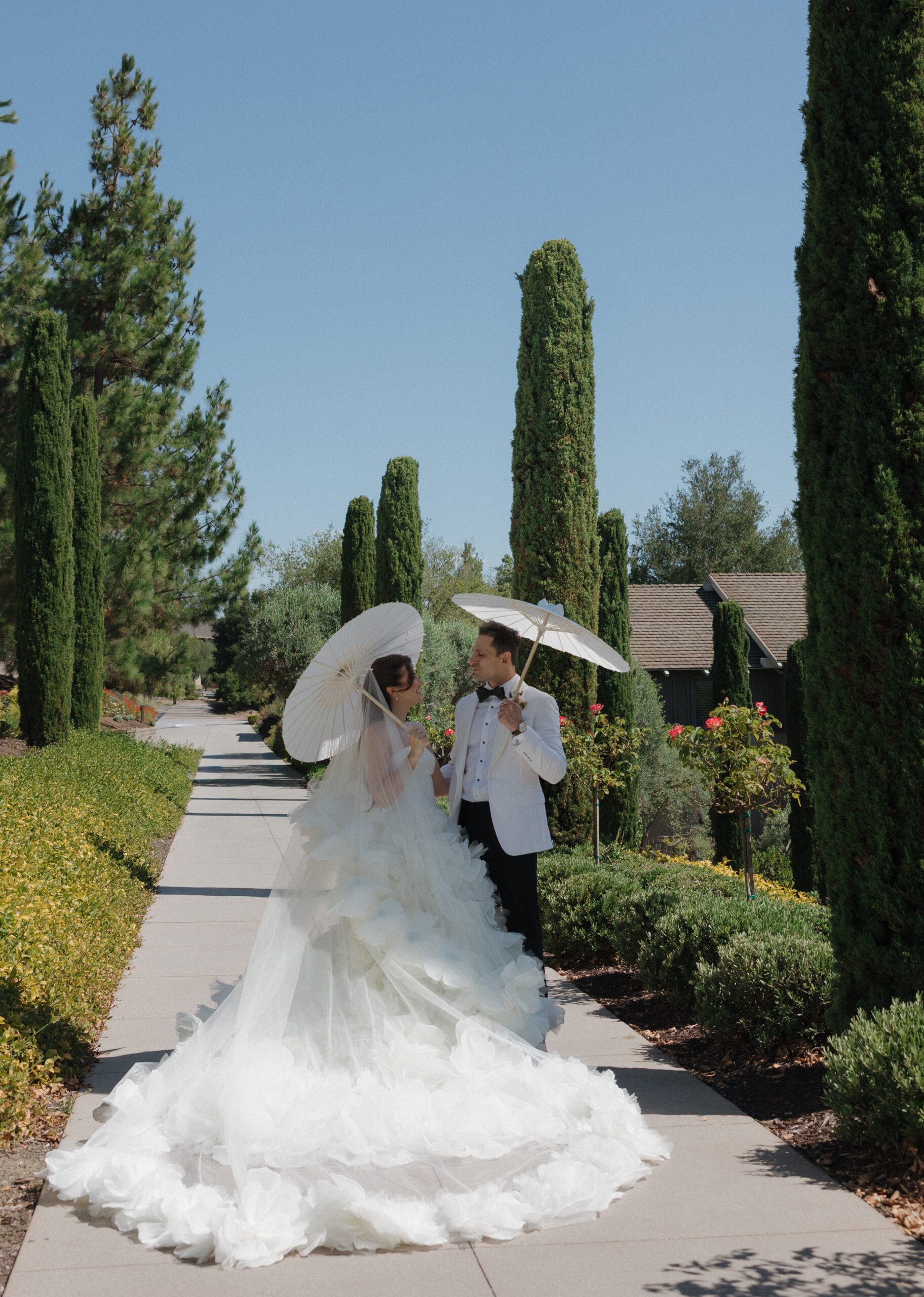 Bride and groom in a garden smiling at each other and holding parasols