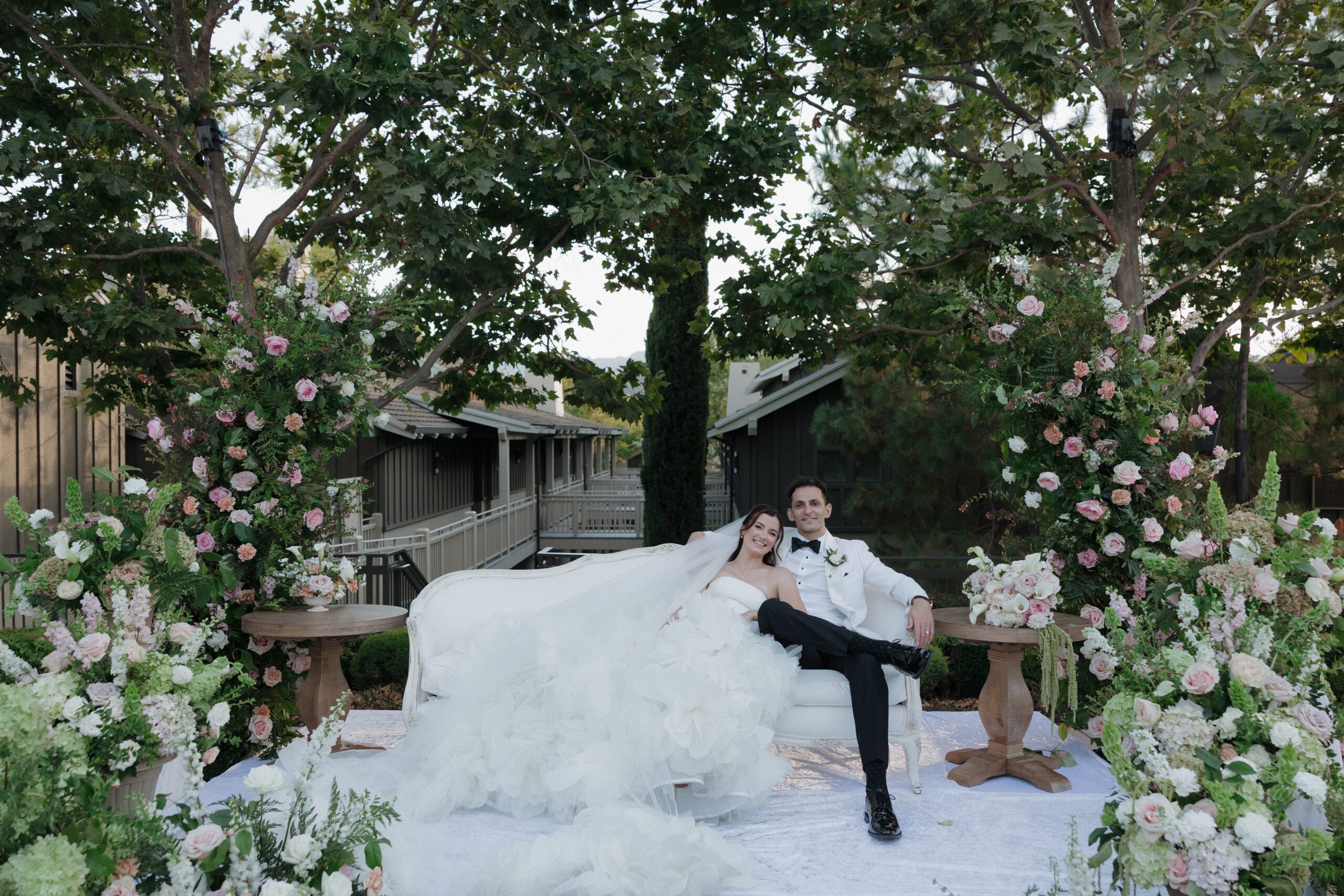 Bride and groom on a couch surrounded by pink and white floral arrangements