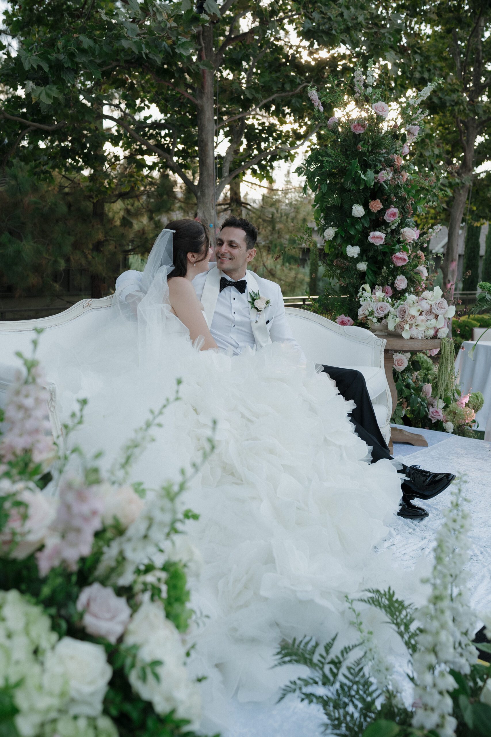 Wedding couple sitting on a couch with pink flowers surrounding them