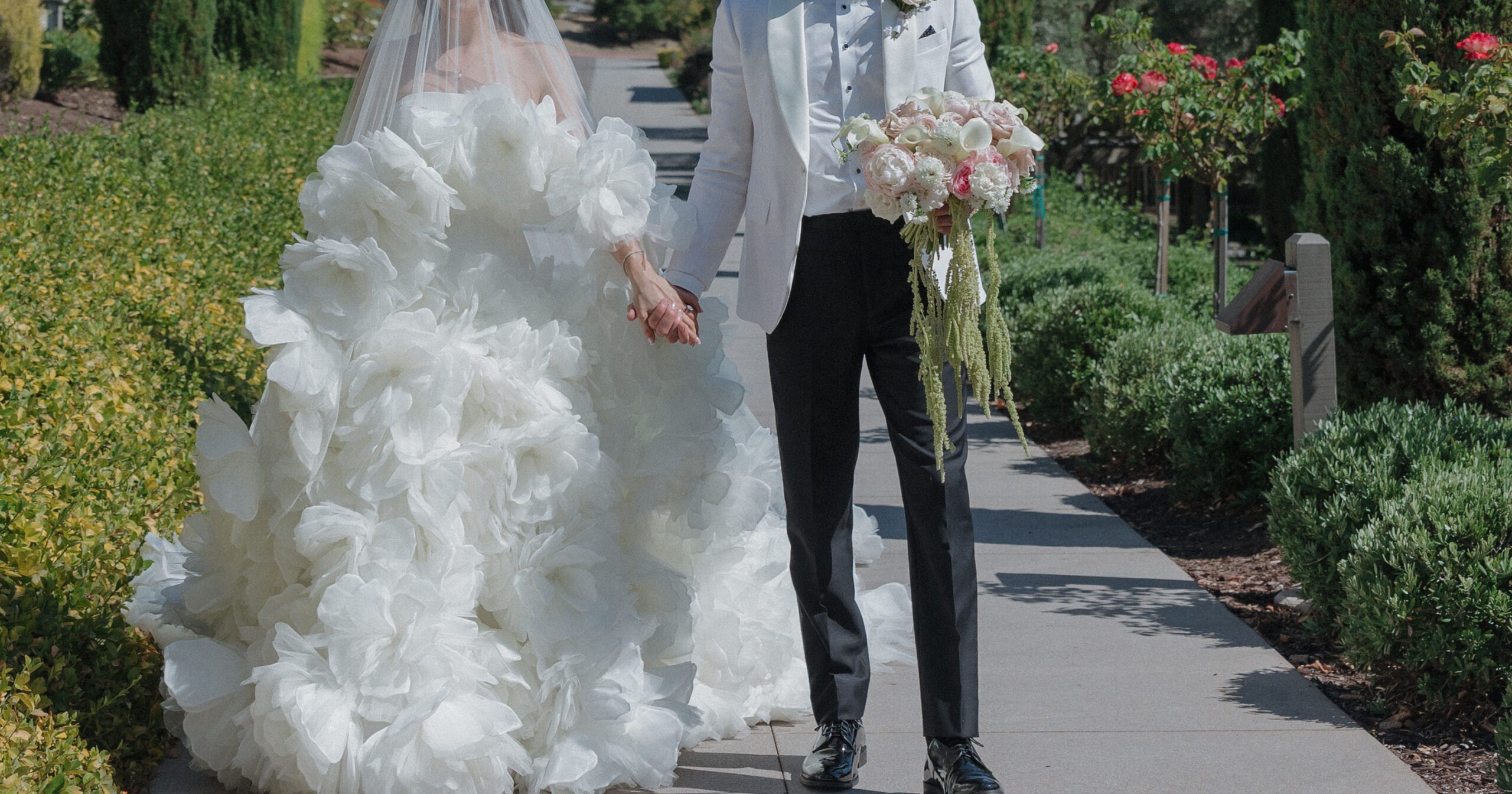 Editorial wedding photo of bride and groom's outfits walking through garden at wedding