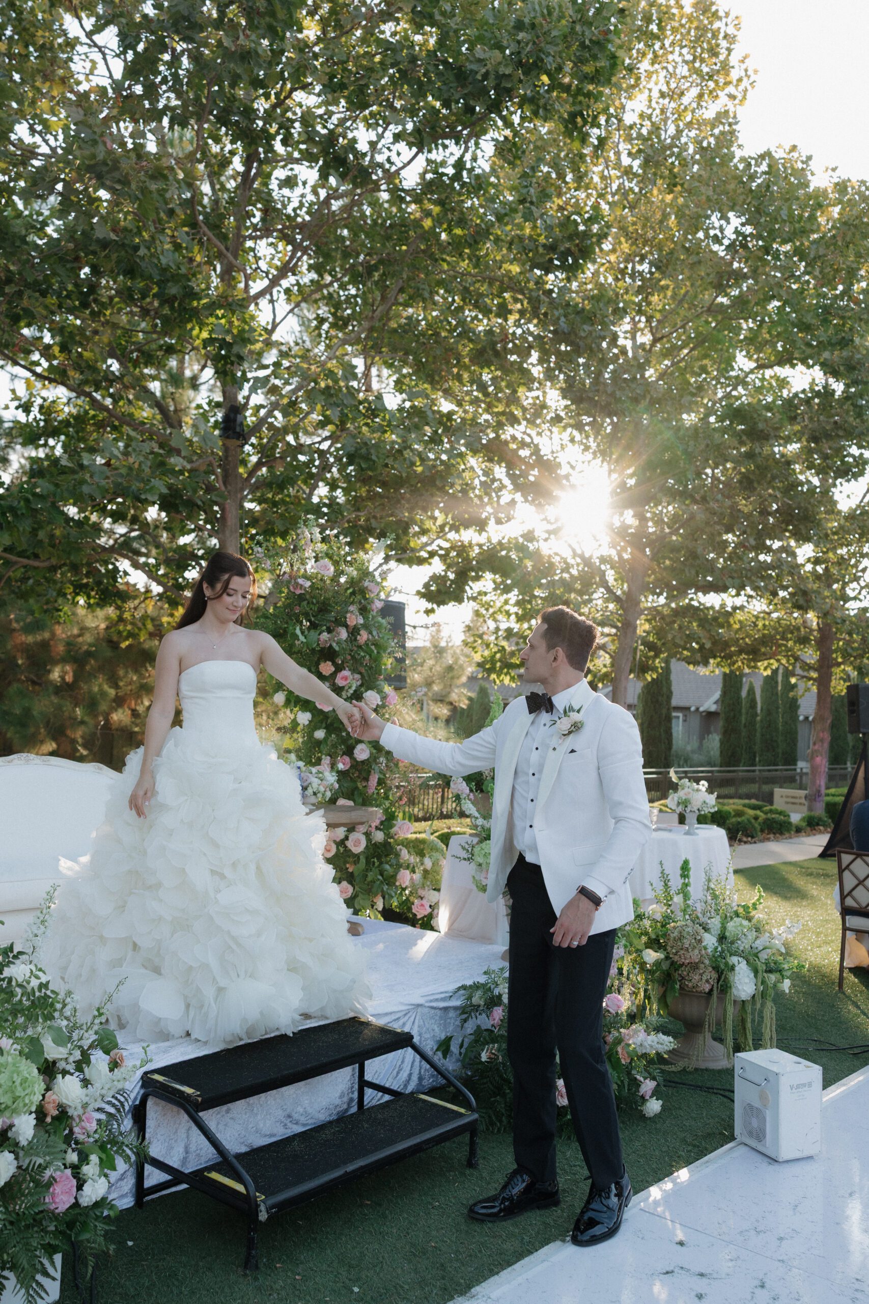 Candid wedding photo of groom helping bride off of the wedding stage