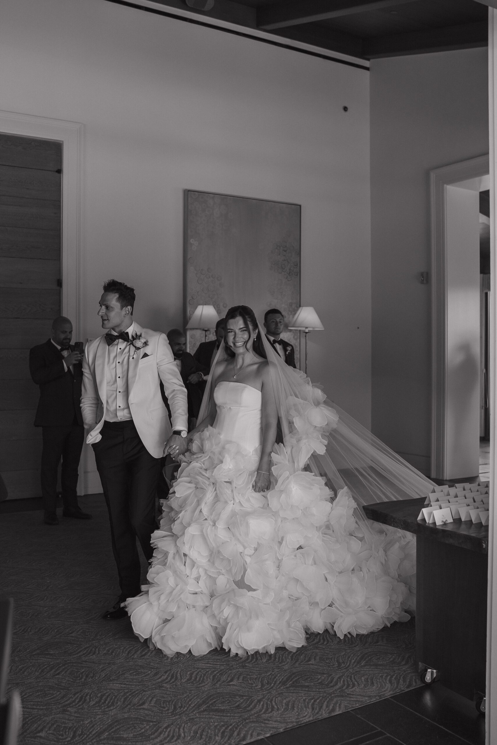 Black and white photo of bride and groom walking through wedding venue
