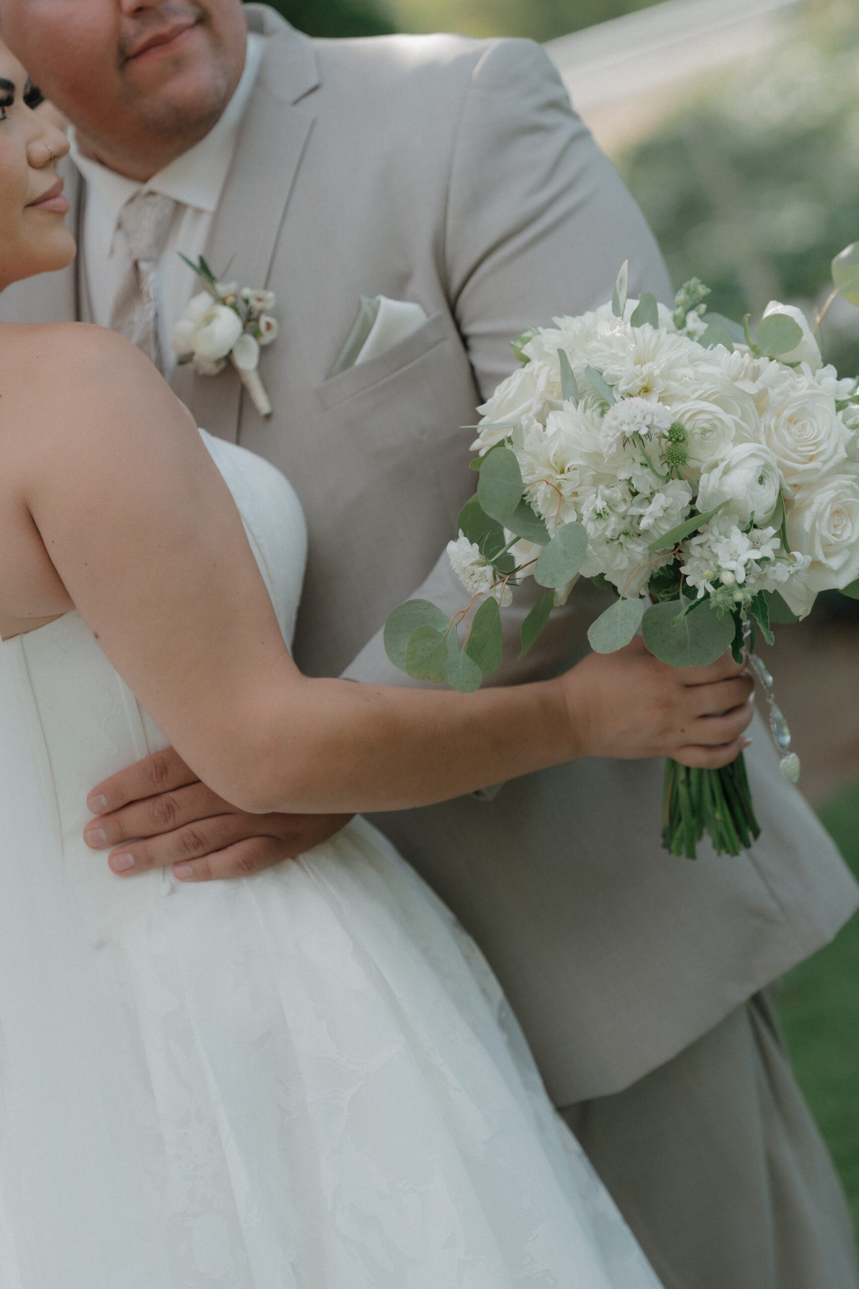 An editorial wedding photo of groom holding bride's waist and bride holding a white wedding bouquet