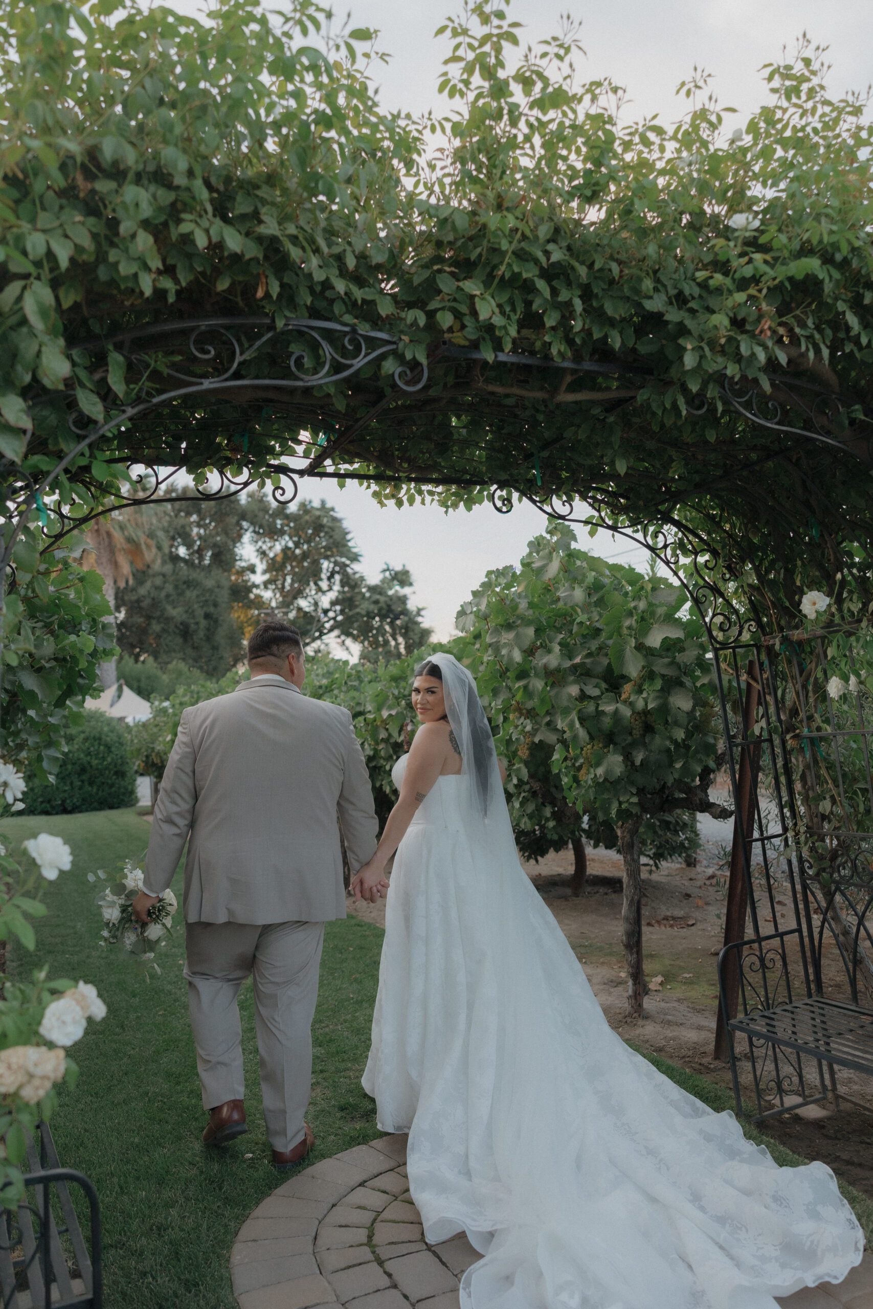 Bride and groom walking through a garden gate with bride looking over her shoulder