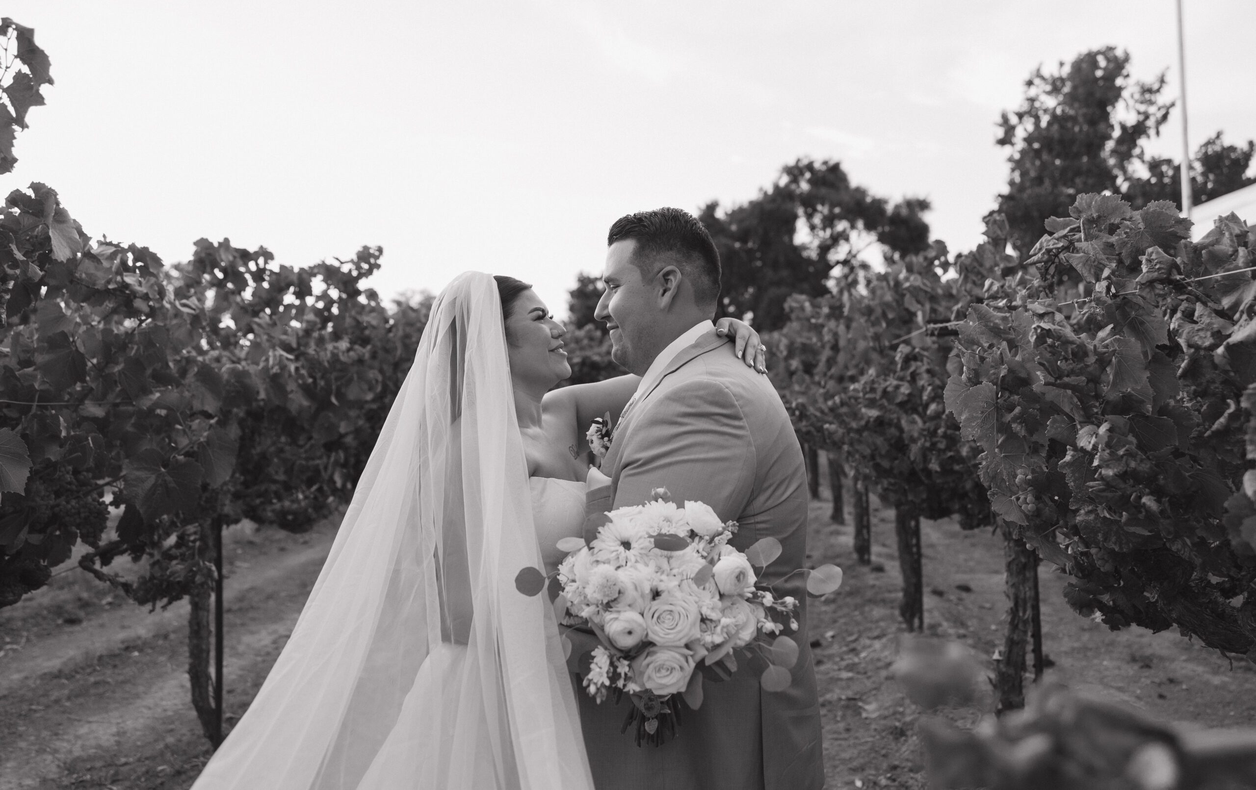 Black and white wedding photo of bride and groom smiling at each other in vineyards