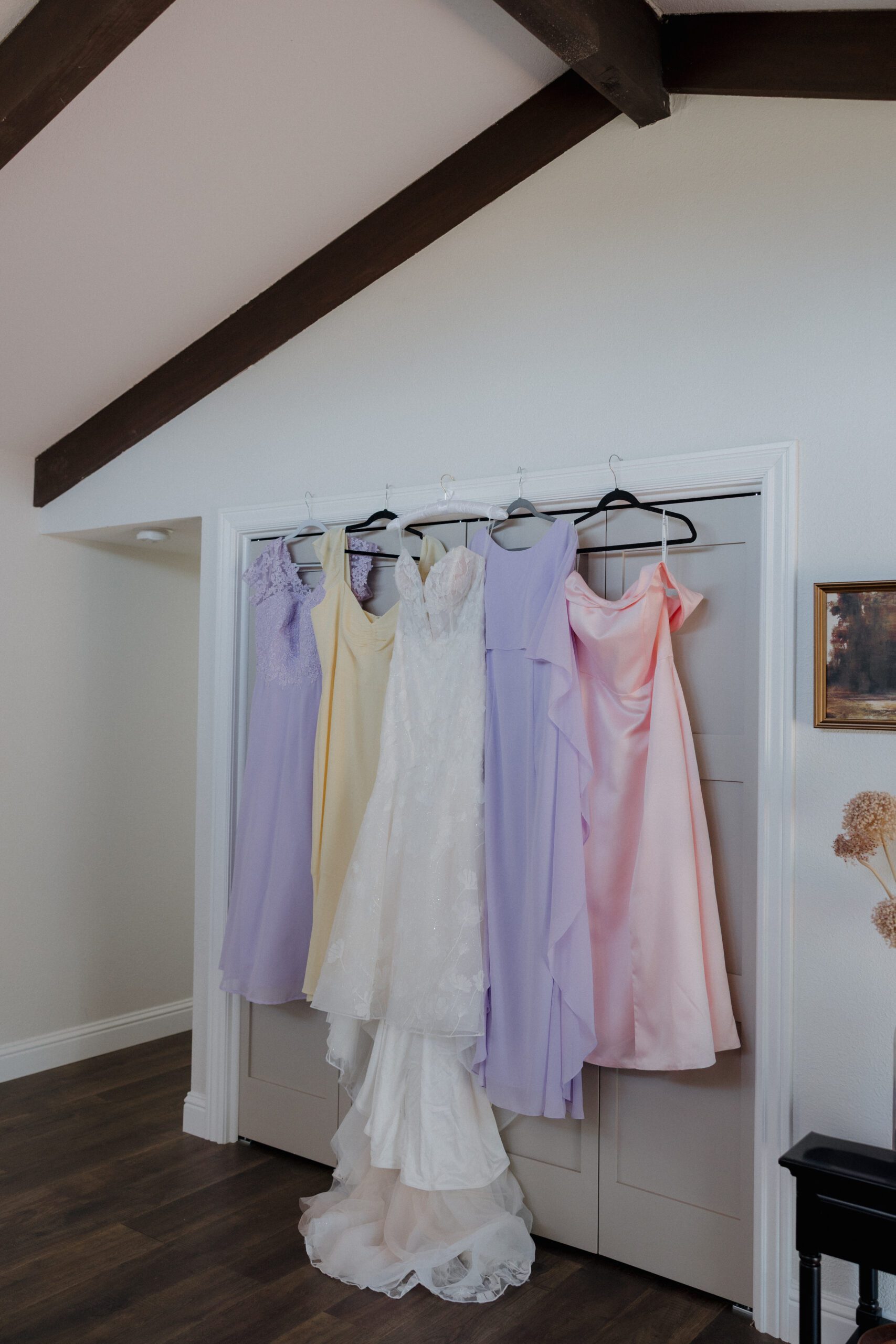 Garden party wedding dress and pastel mismatched bridesmaid dresses hanging up together