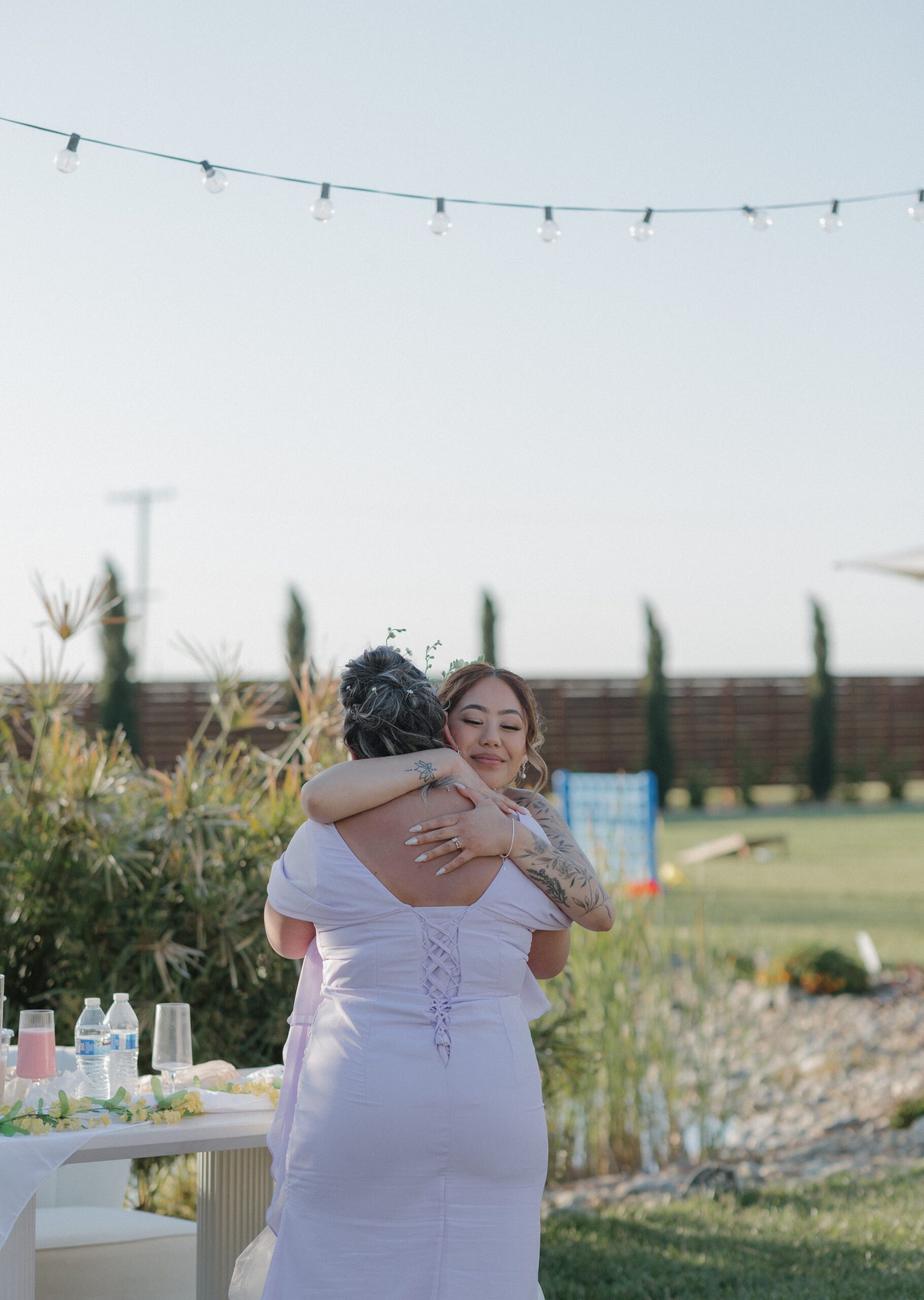 Bride hugging a wedding guest in a pastel purple wedding guest dress for her garden party wedding