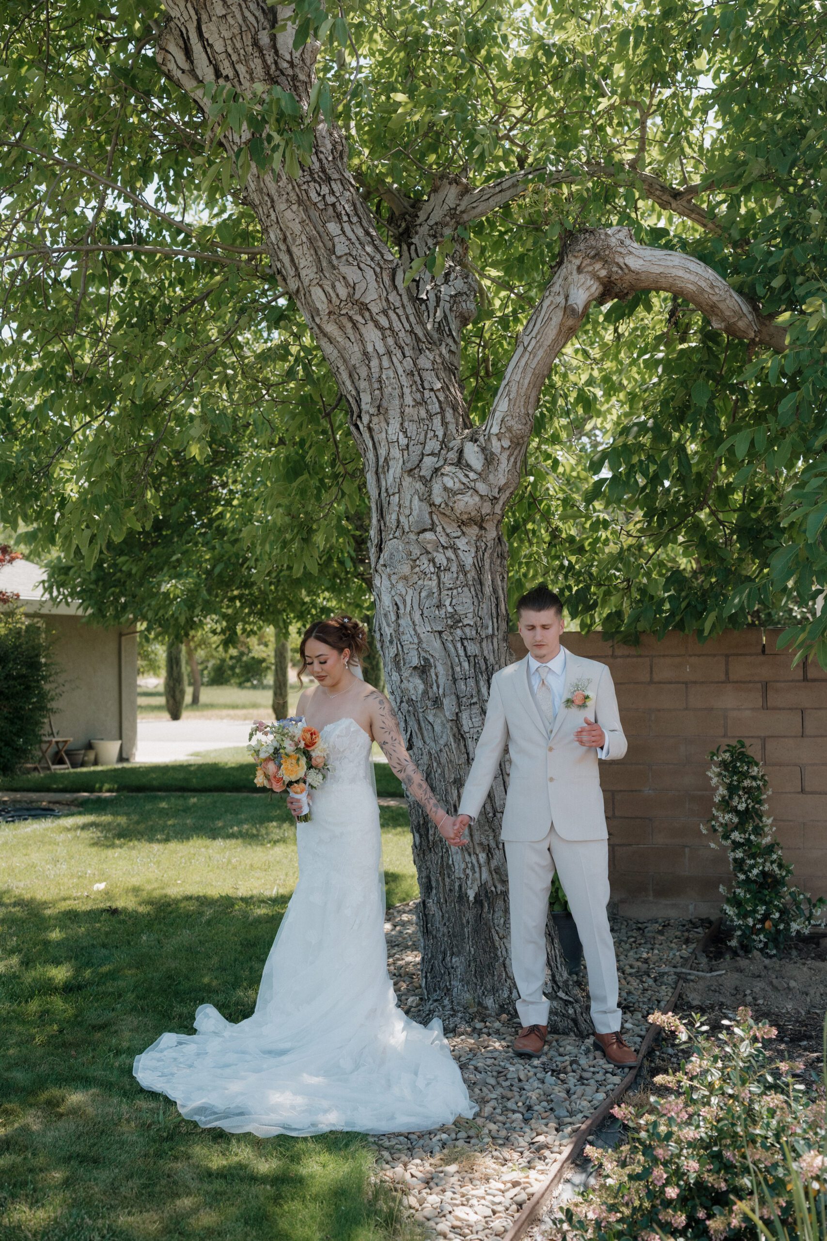 A bride and groom sharing a private first touch underneath a tree before their wedding ceremony