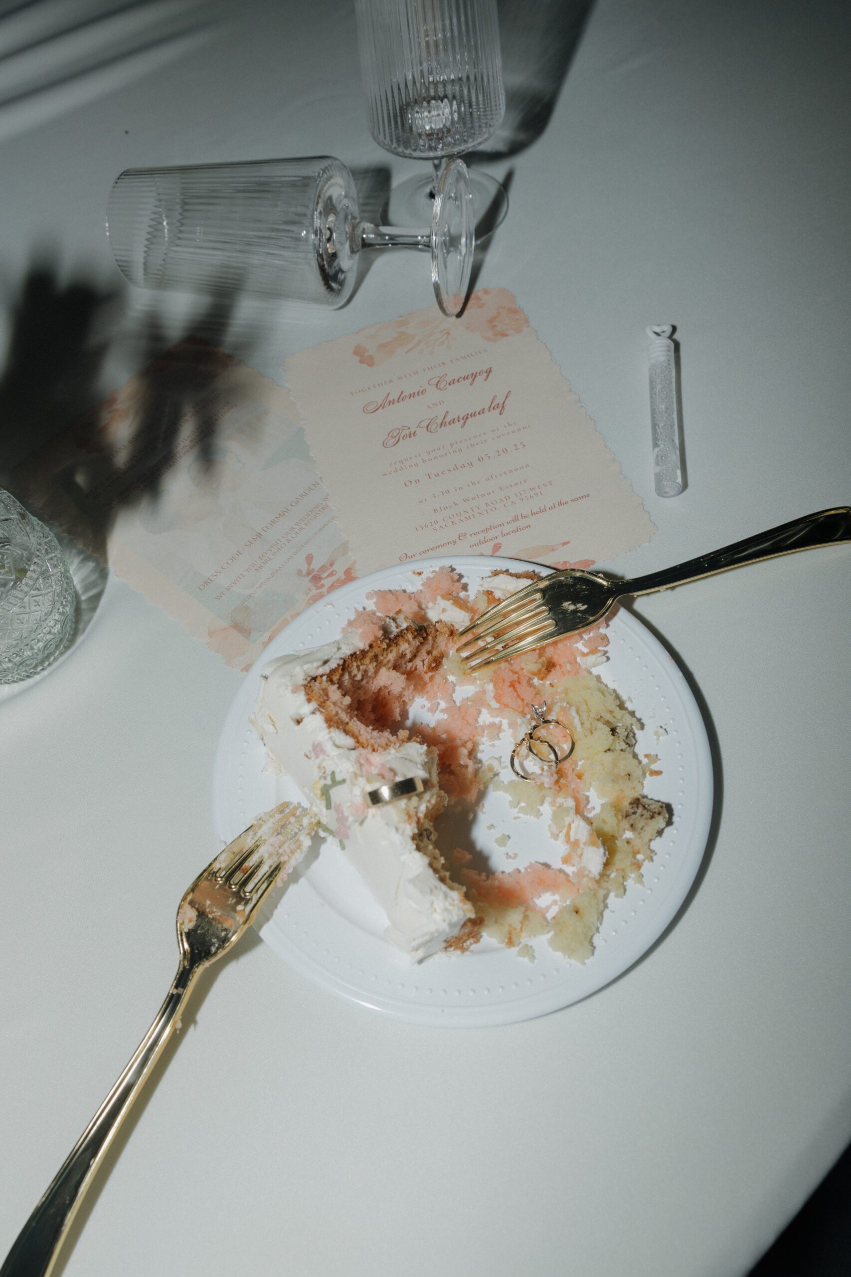A wedding reception flat lay photo with wedding cake, wedding rings, and champagne flutes