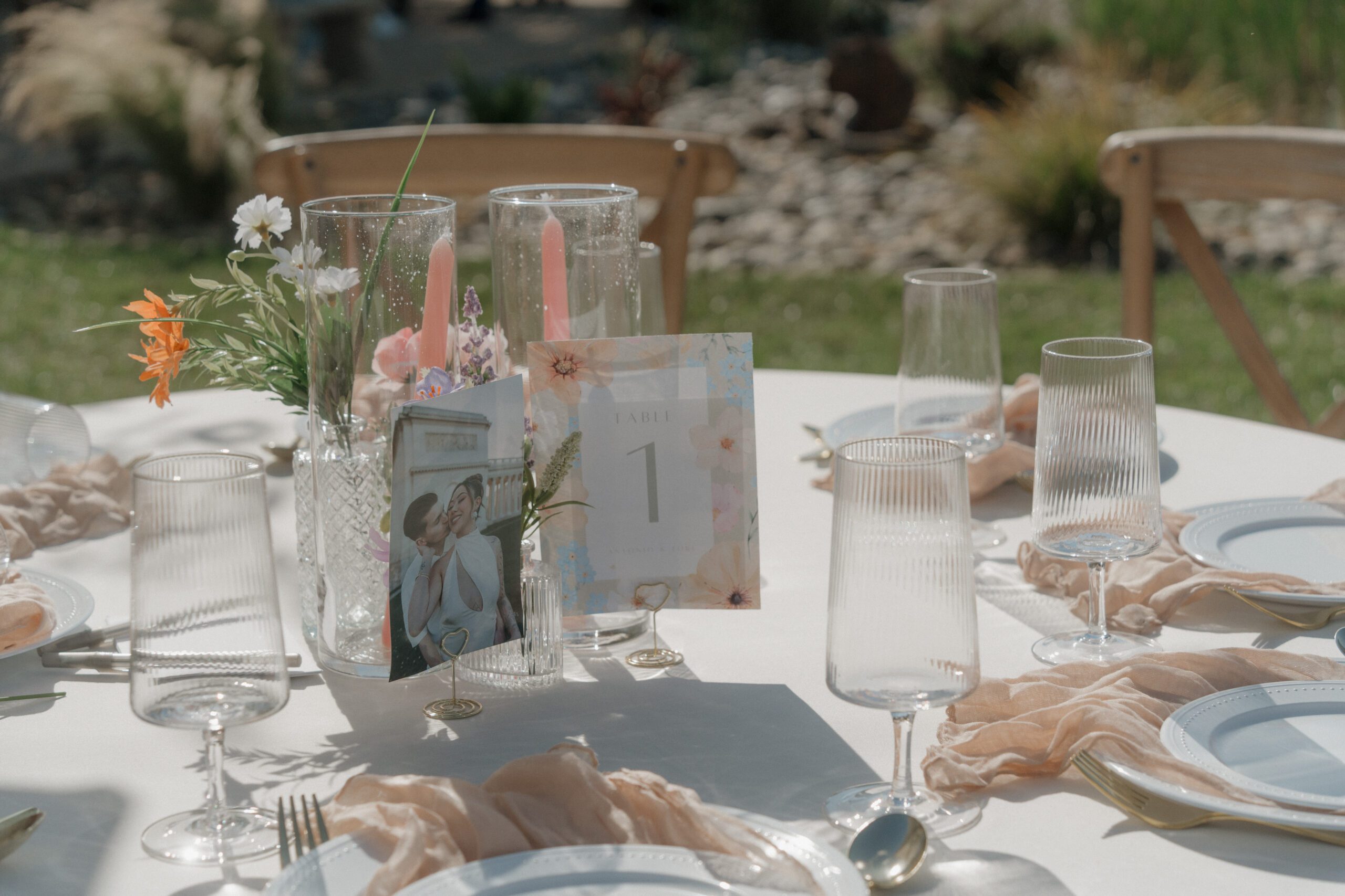 A table setup for an outdoor wedding reception at a garden party wedding with pink napkins and floral table numbers