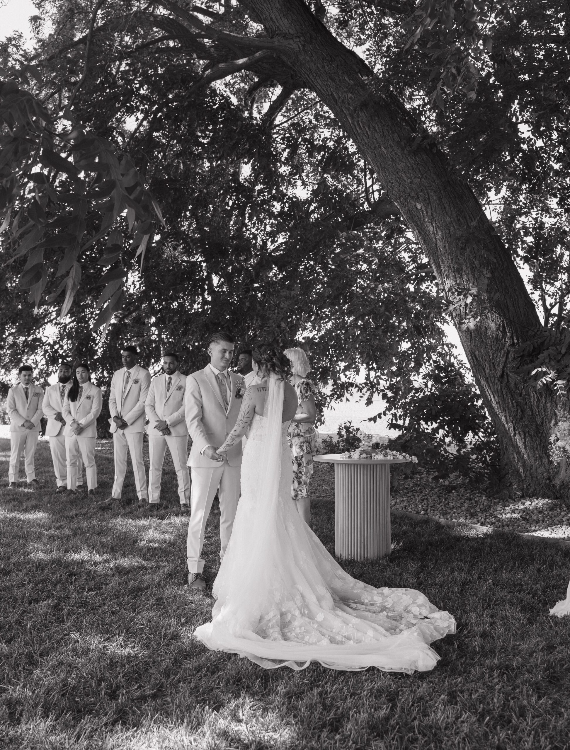 Black and white wedding photo of bride and groom's outdoor wedding ceremony under a tree