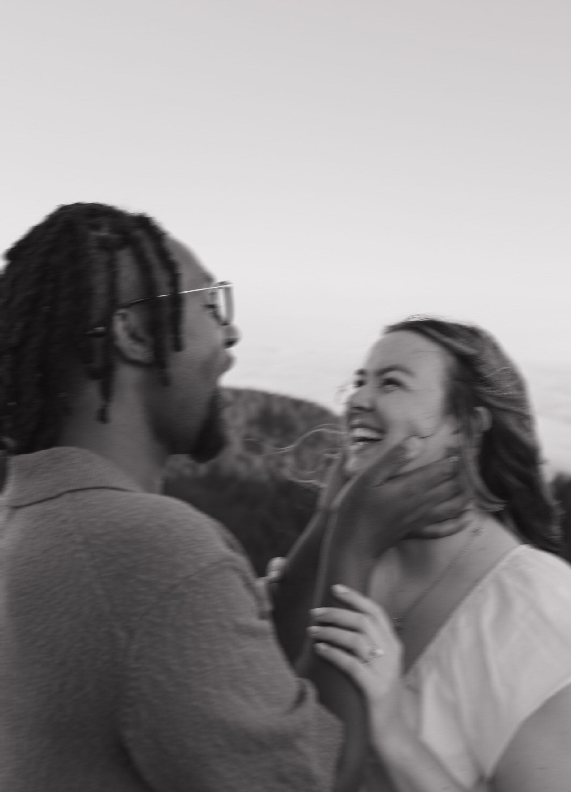 A blurry photo of a man holding his fiancees face while she laughs during engagement photos