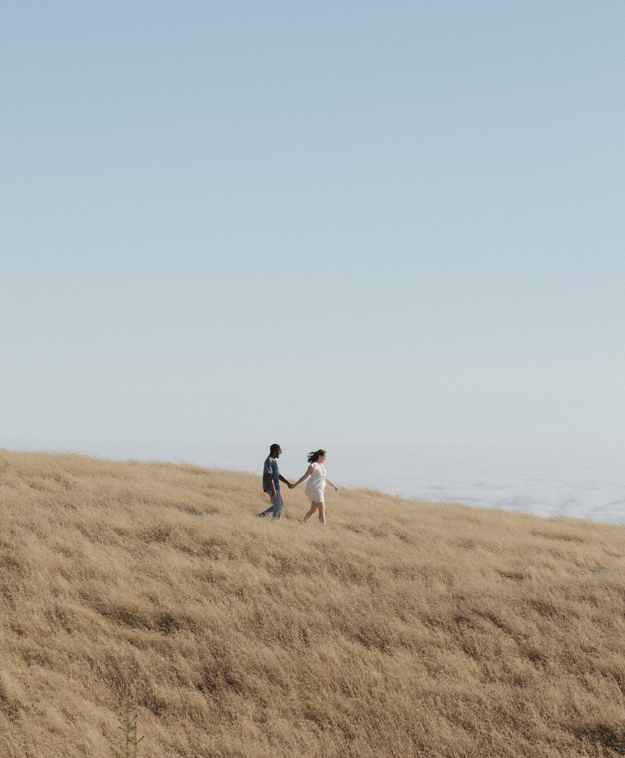 A wide-lens photo of couple holding hands and walking down a hill at Mt. Tamalpais