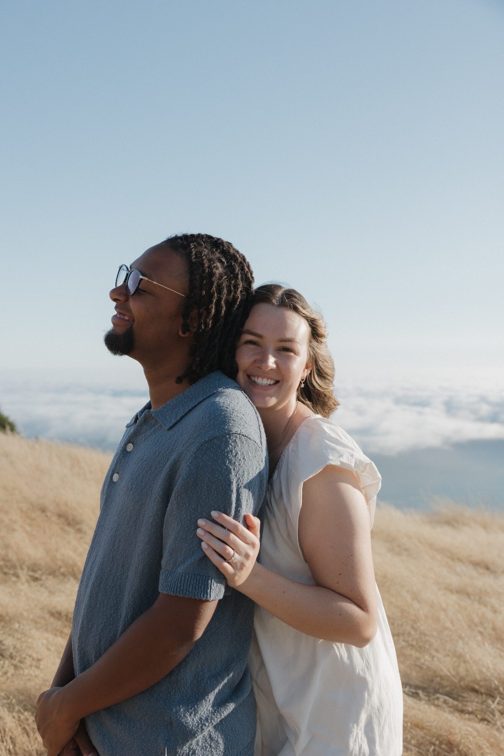 A girl hugging her fiancé from behind and showing off her ring during engagement photos