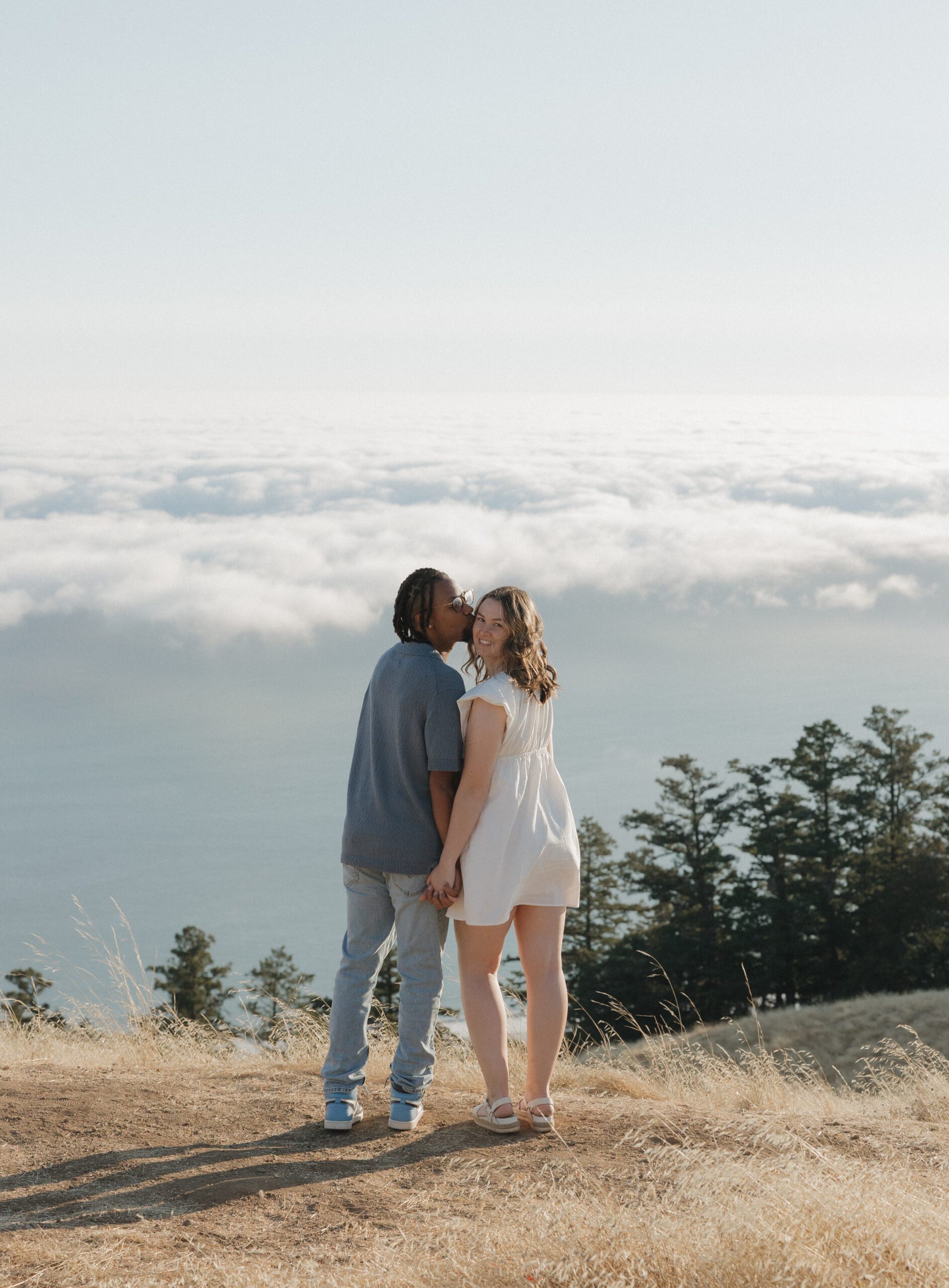 A man kissing his fiancee on the cheek overlooking the view from Mt Tamalpais