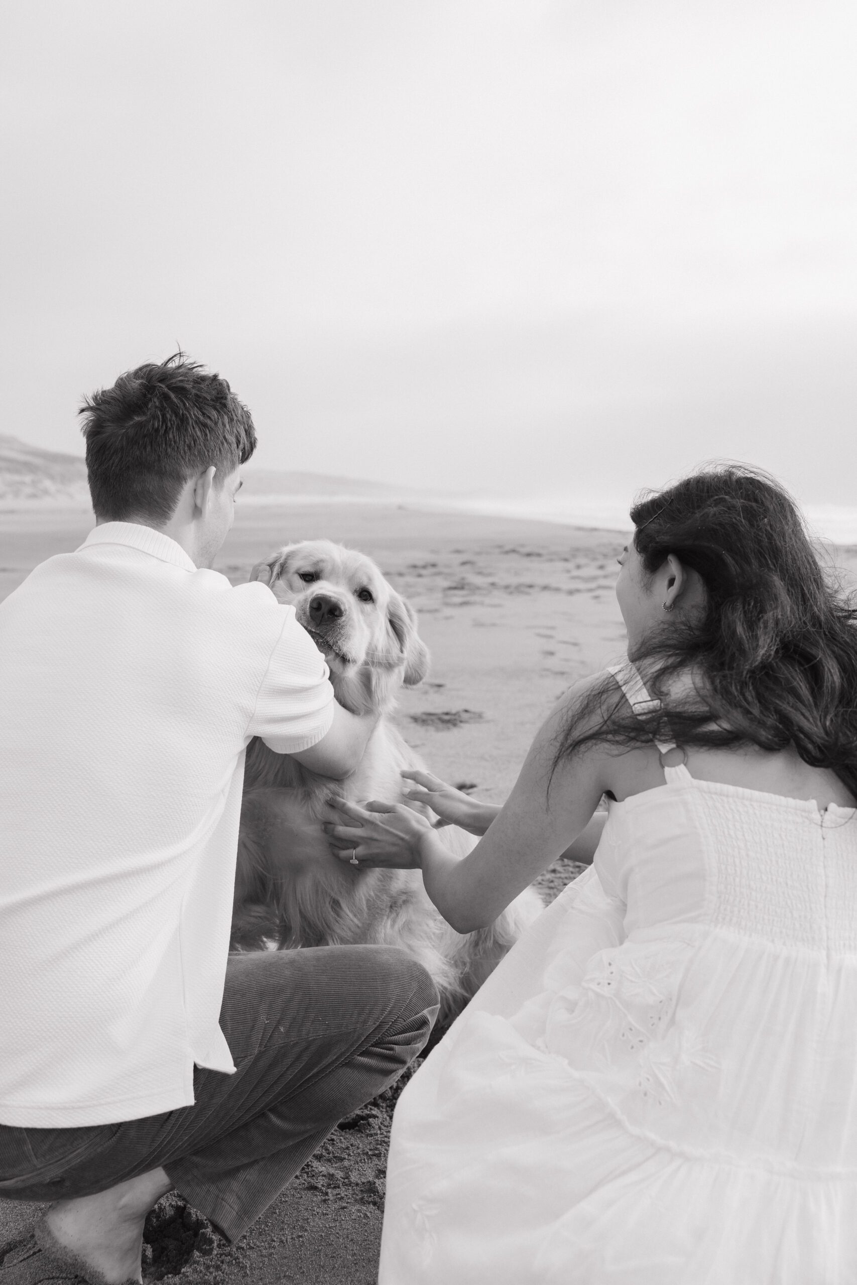 Black and white engagement photo of couple petting their dog